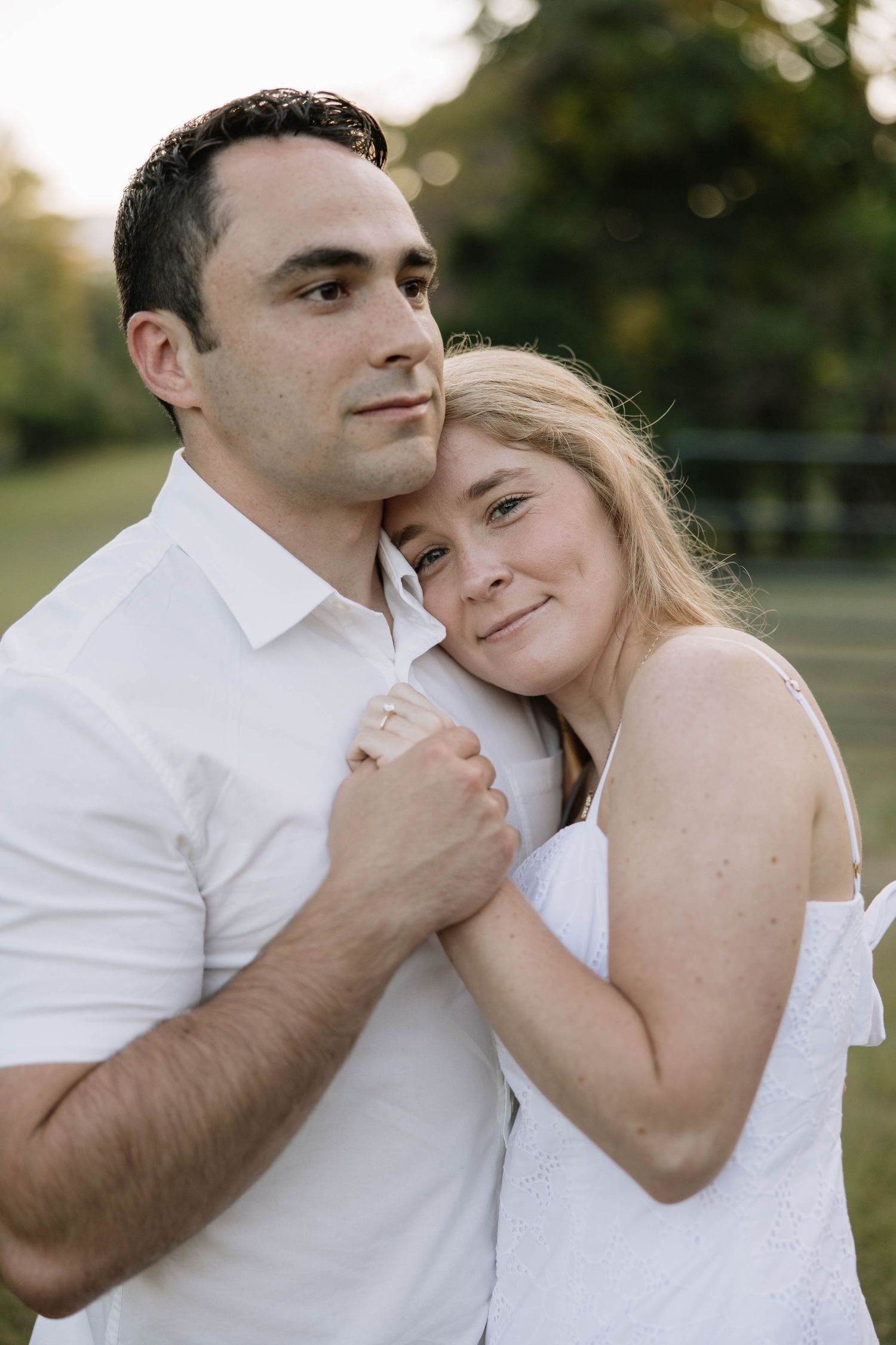 A couple in white clothing embracing tenderly in an outdoor setting.