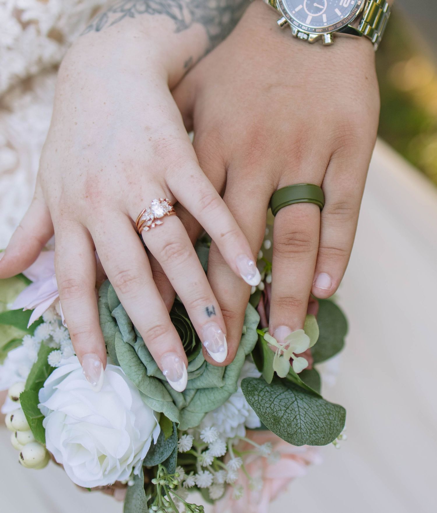 Close-up of wedding rings and white floral bouquet with pearl details.