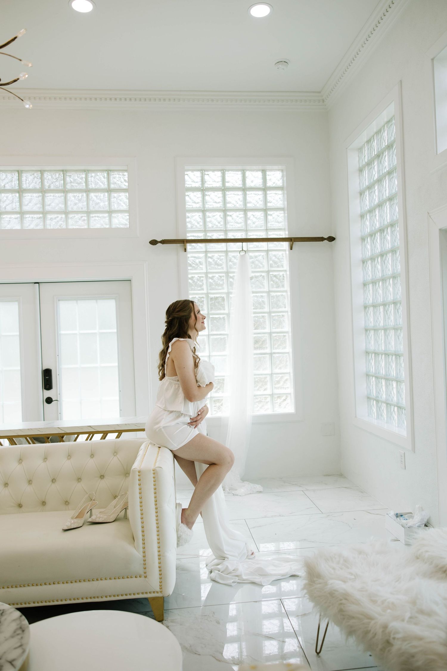 A bright white room with glass block windows and a tufted chaise lounge creates an ethereal boudoir setting.
