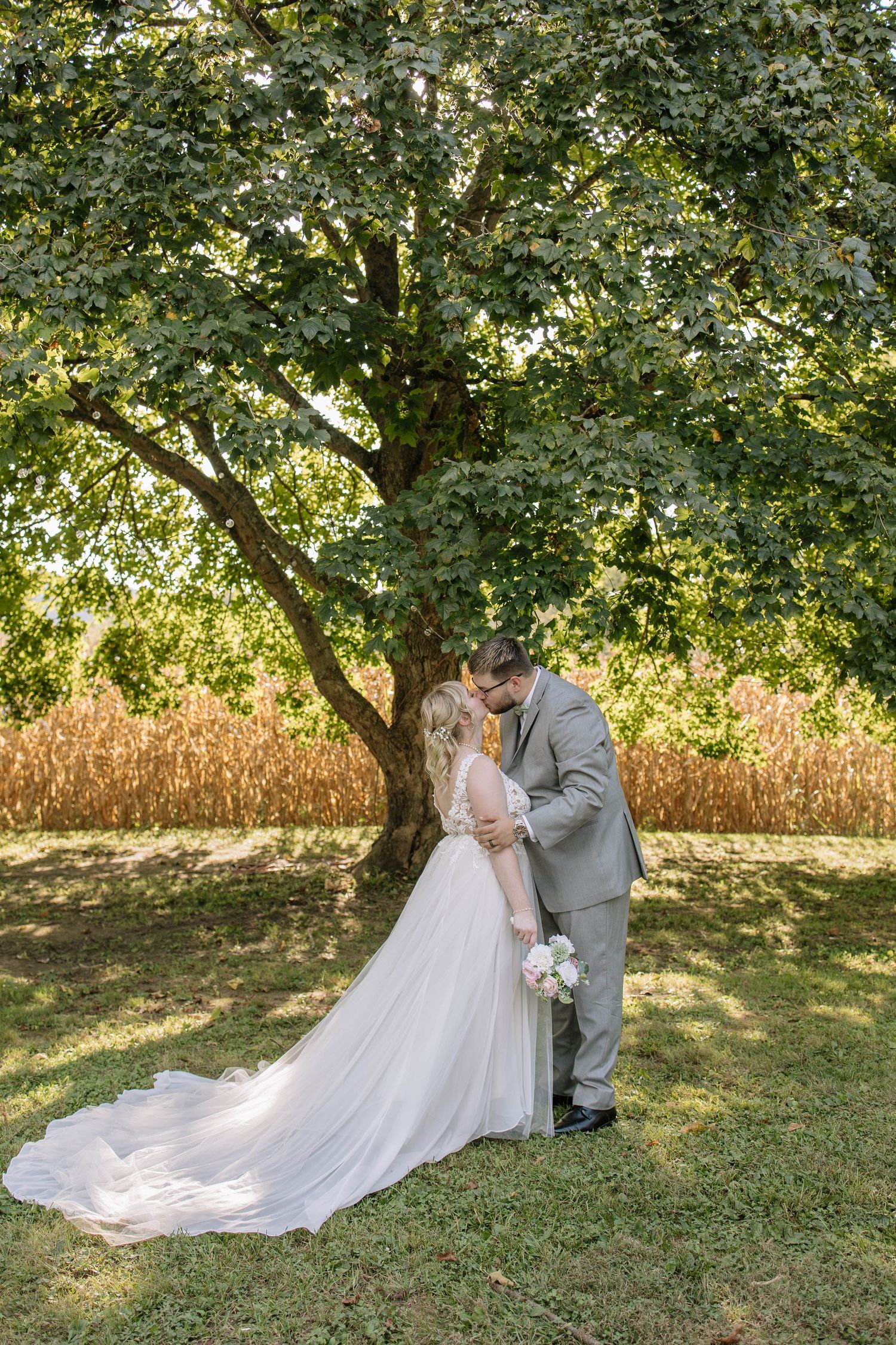 A romantic wedding photoshoot under a tree with a flowing white dress and gray suit.