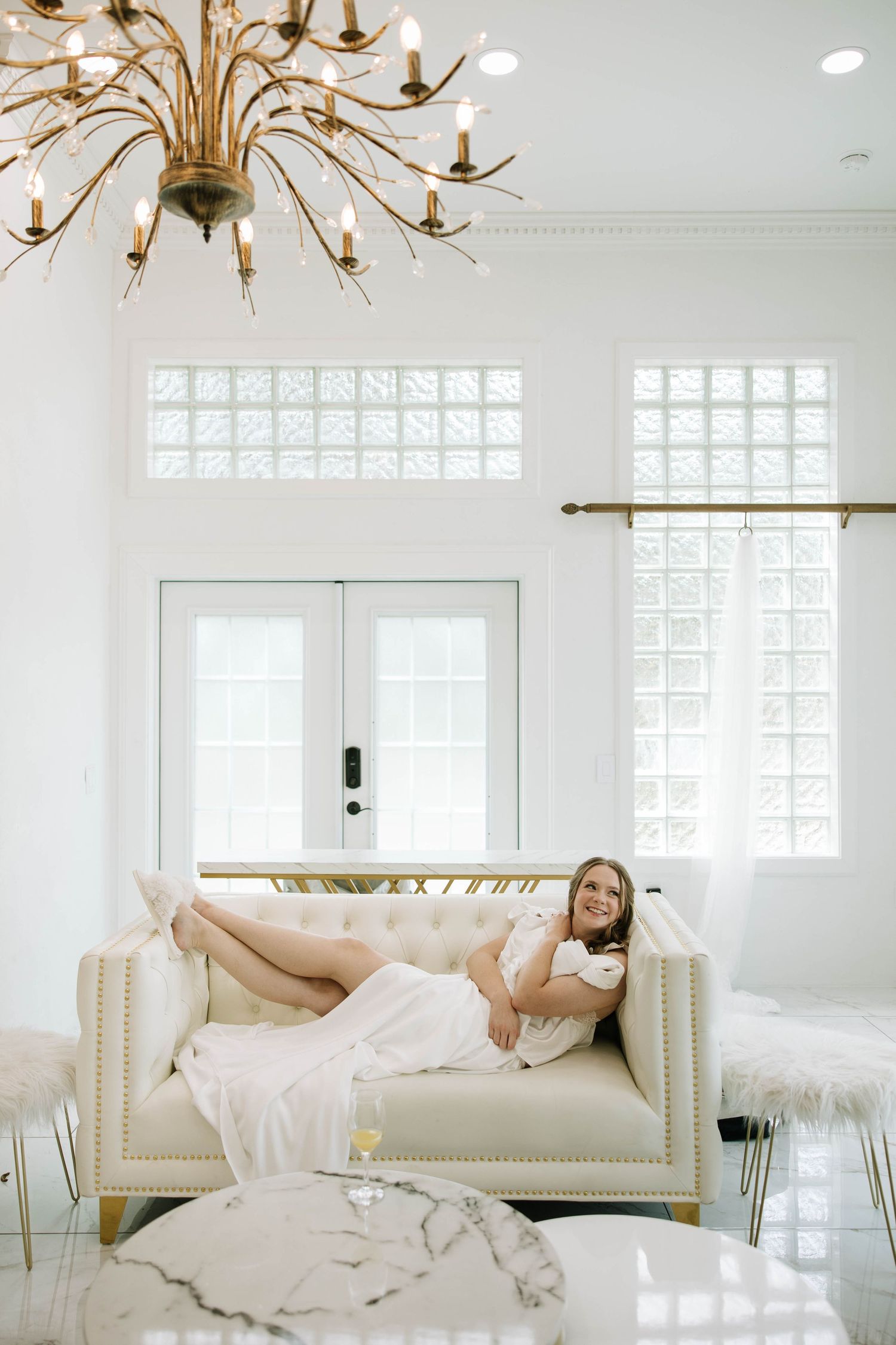 Elegant living room interior with gold chandelier, white French doors, and cream-colored sofa against bright white walls.