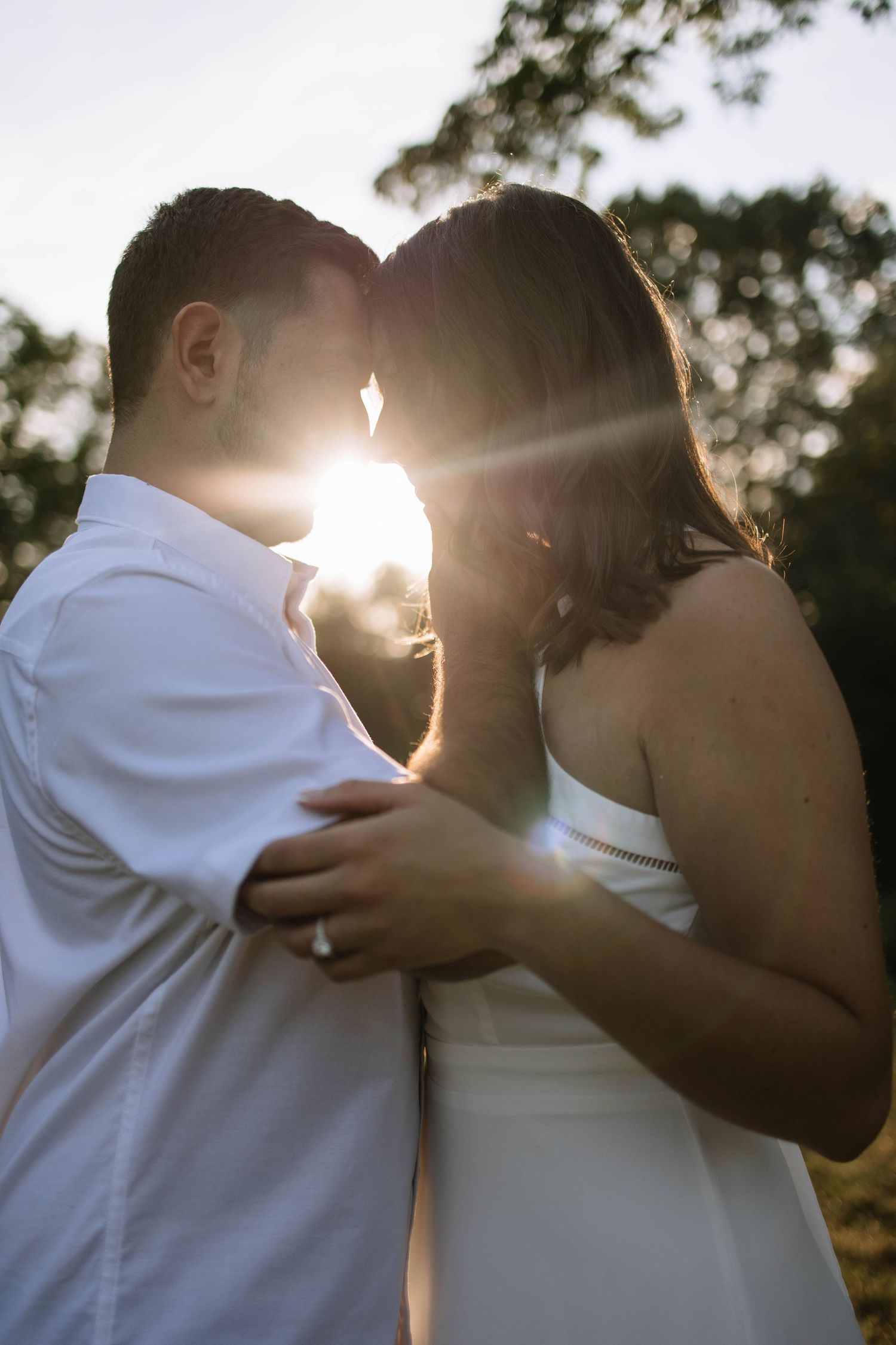 Romantic couple embraces in golden sunset light during outdoor photo session.