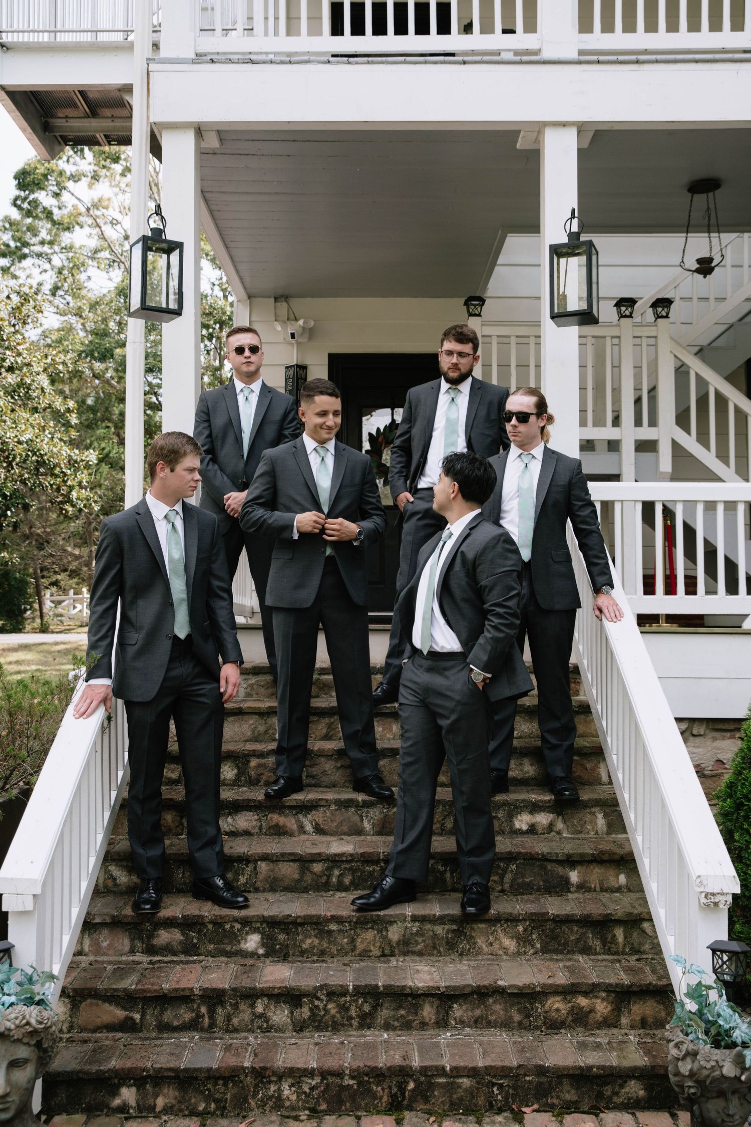 Groomsmen in dark suits pose playfully on stone steps of a white porch in a candid wedding photo sequence.