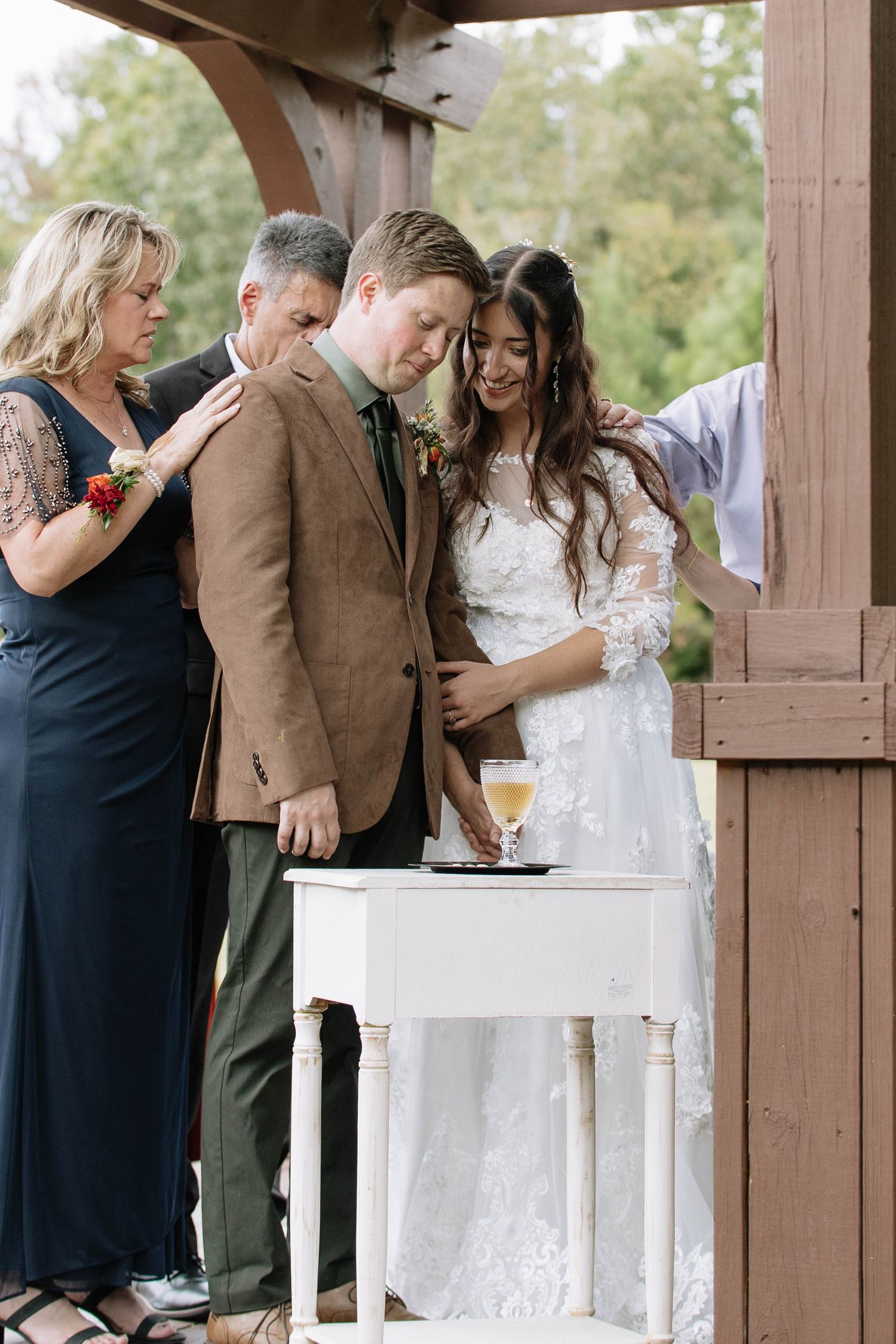 Wedding ceremony participants gathered around white table under wooden pergola.