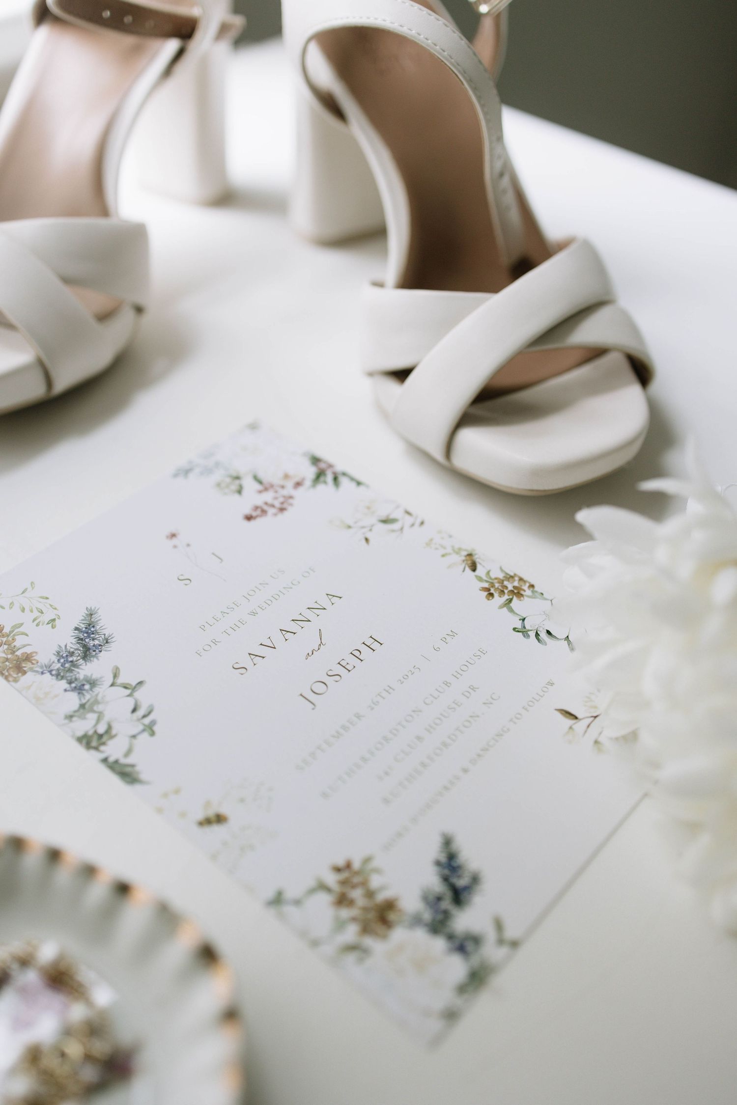 Elegant wedding invitations with delicate floral designs and white heels arranged on a light surface.