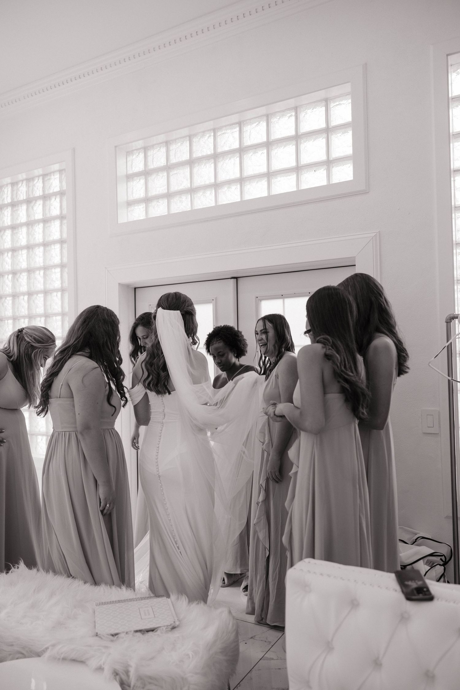 Black and white image of bridesmaids in matching dresses lined up against a white wall with windows.