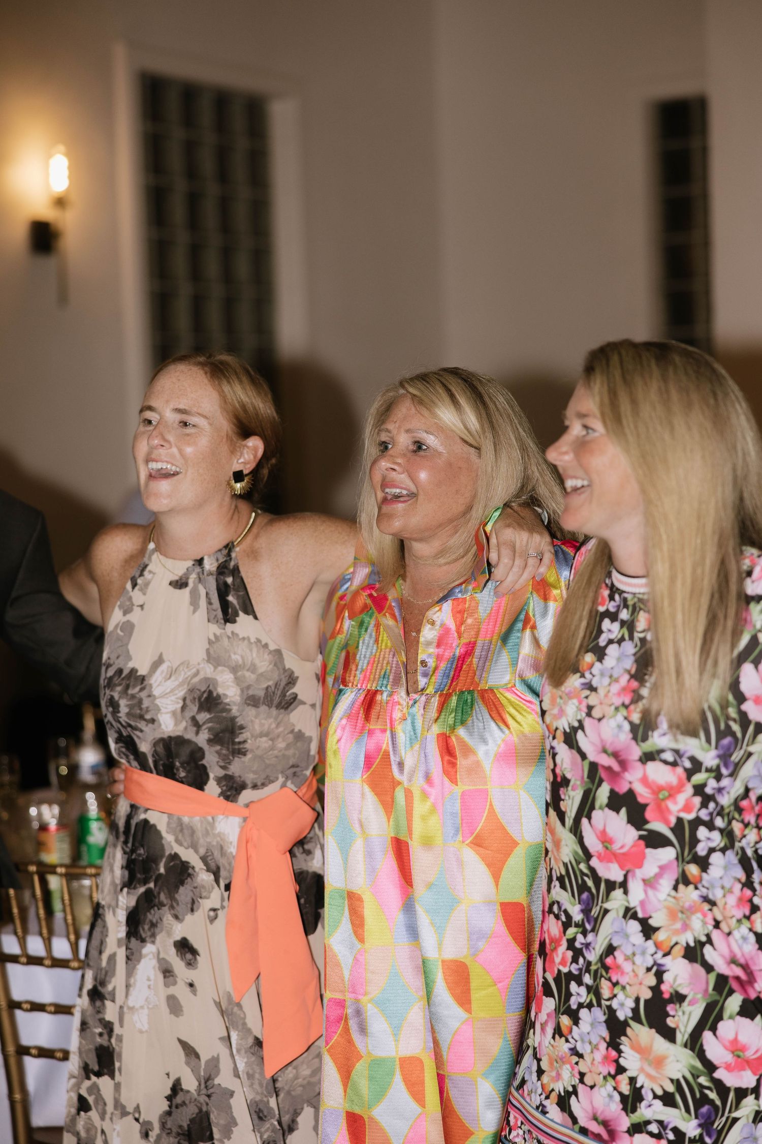 Wedding guests in colorful floral dresses laughing and enjoying the celebration.