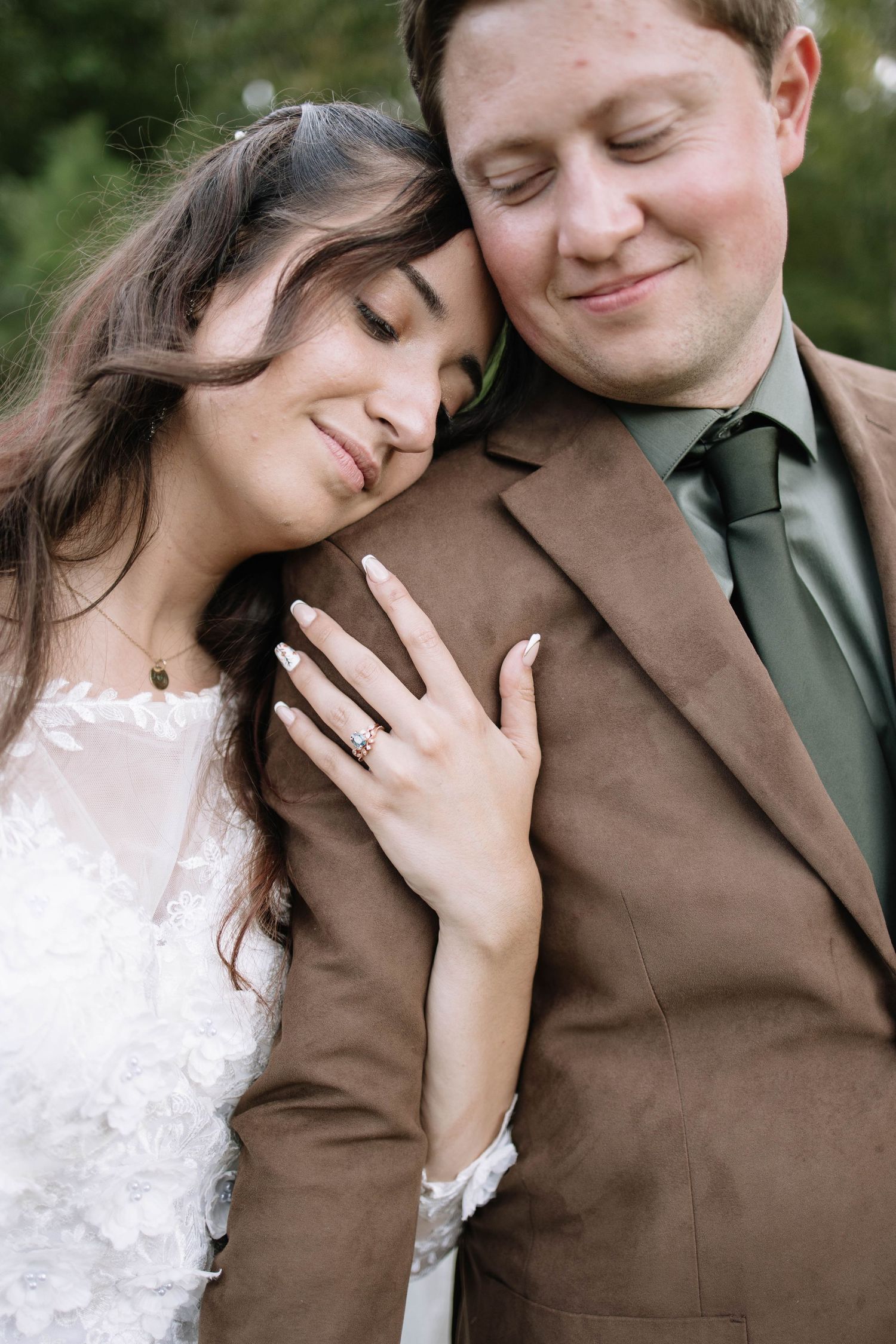 A tender moment captured between a couple in wedding attire against a natural outdoor backdrop.
