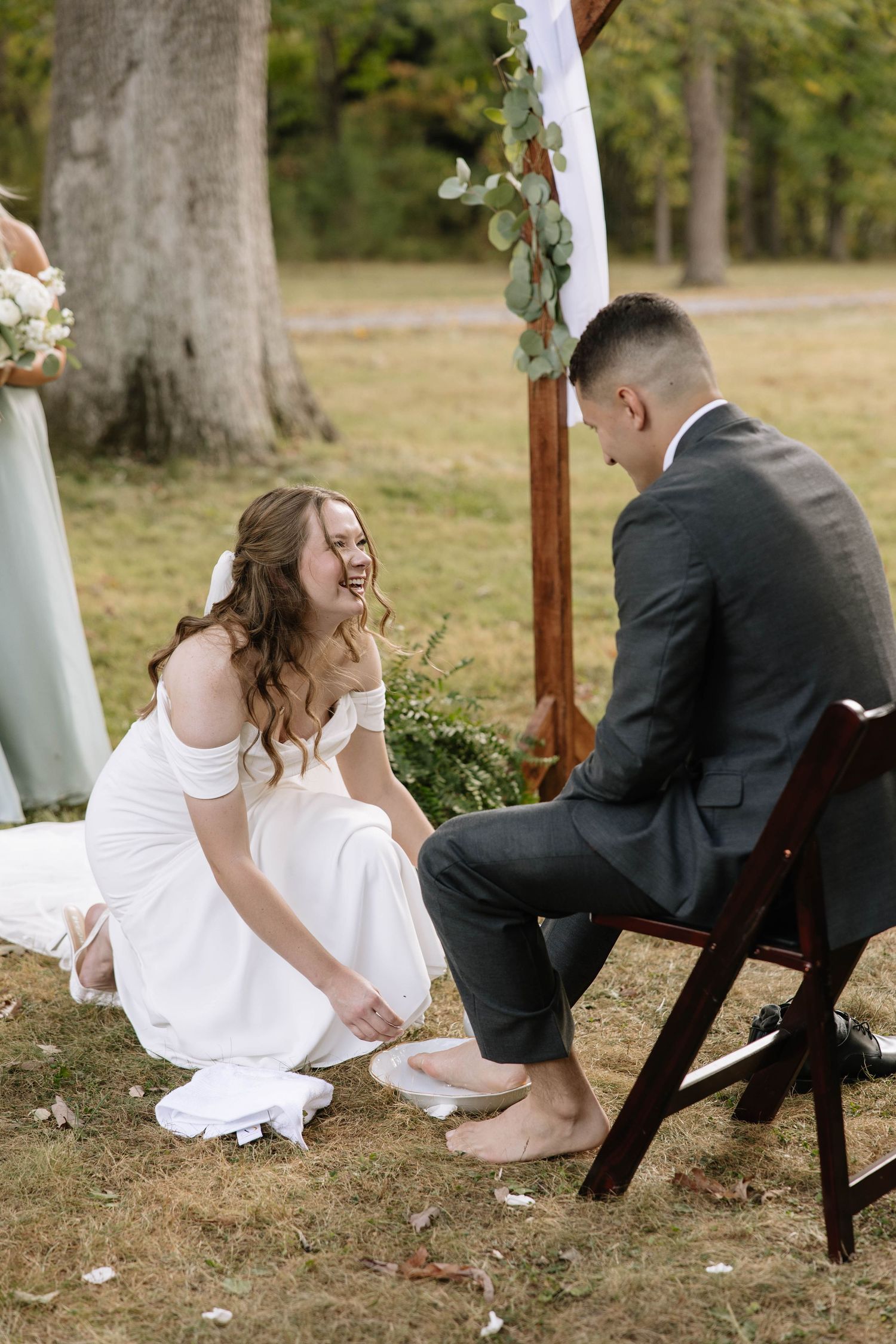 A couple shares a joyful moment during their outdoor wedding ceremony as they participate in a foot washing ritual.