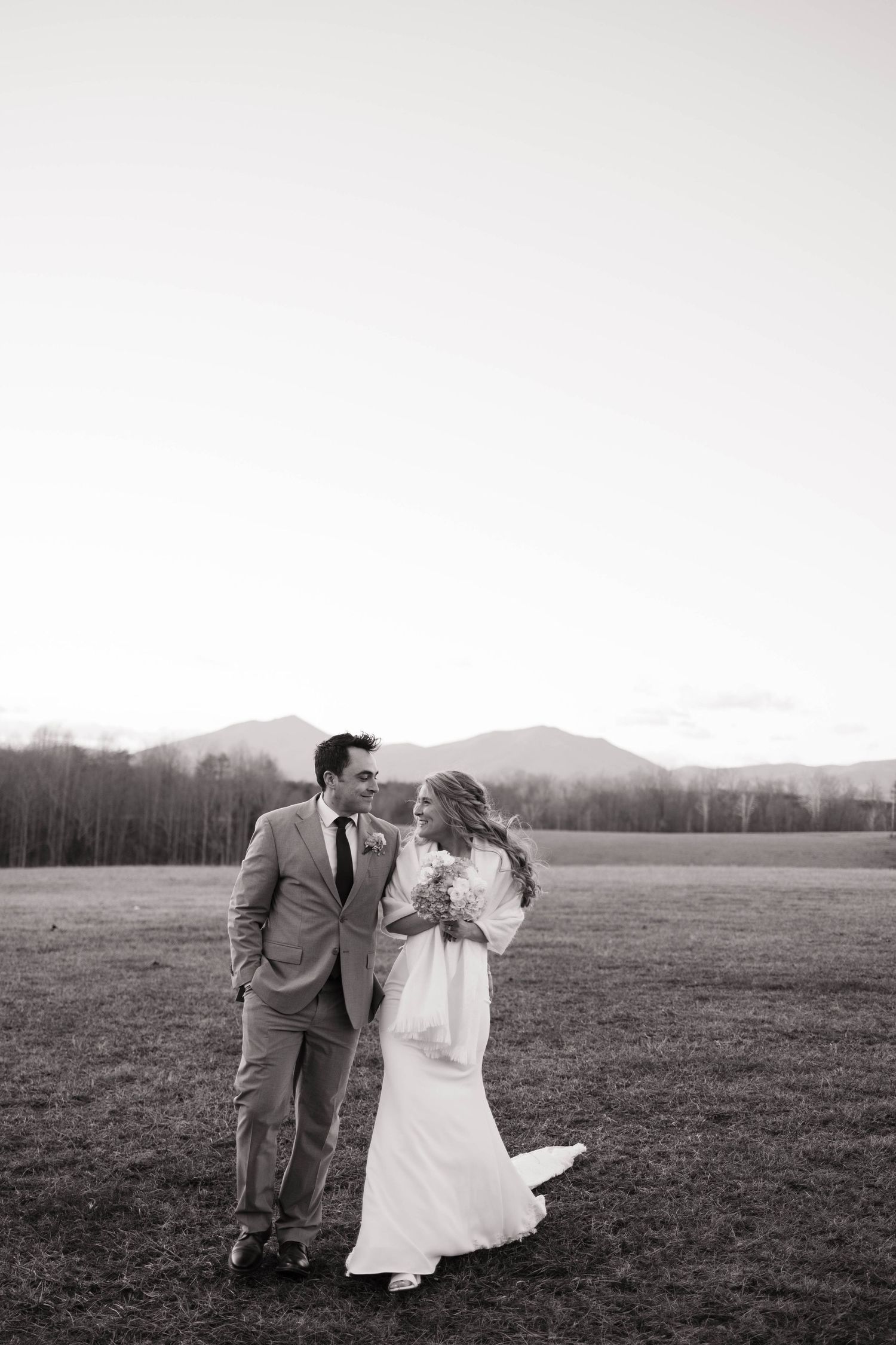 Black and white wedding portrait of couple in open field at dusk.