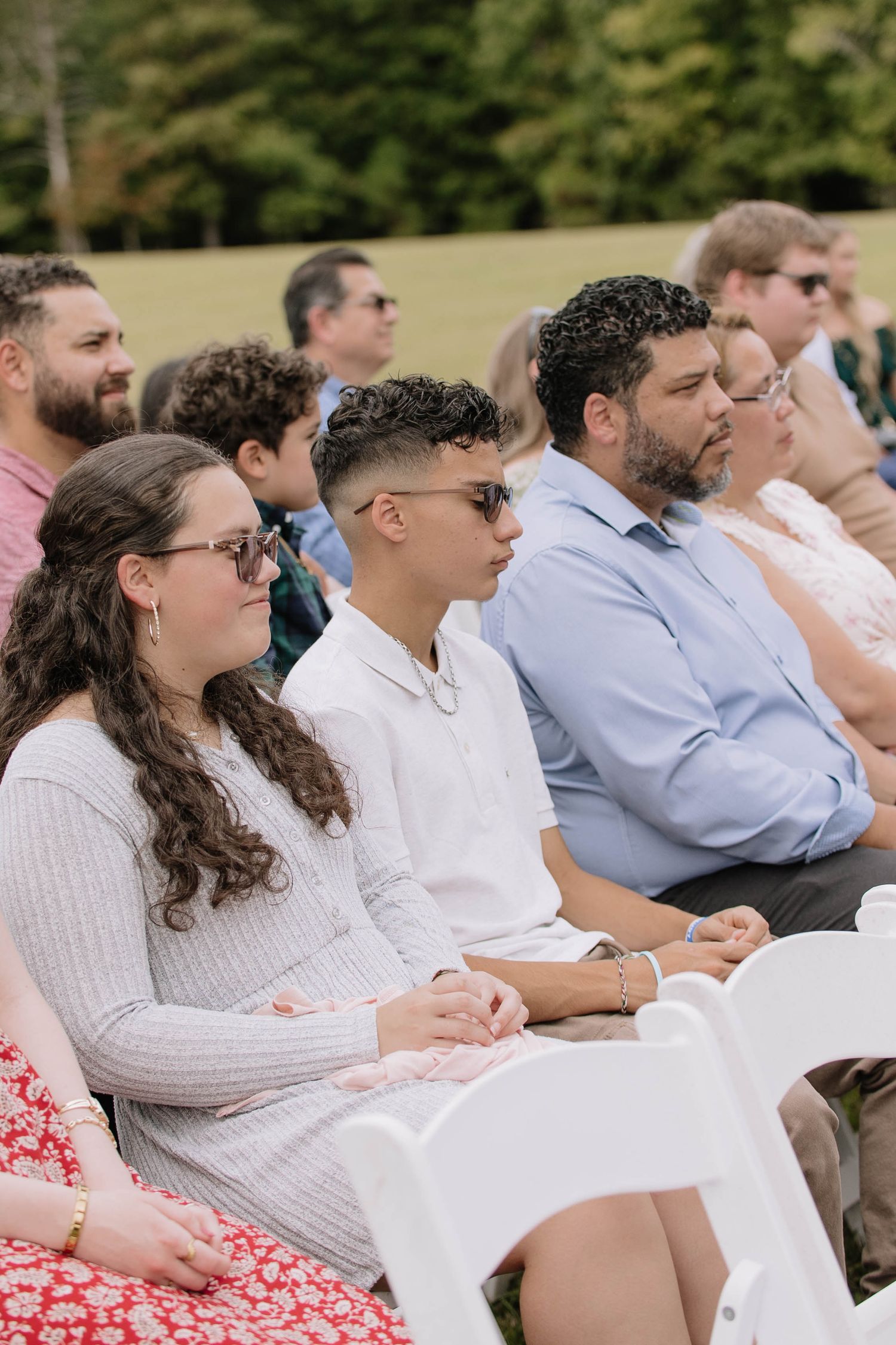 Wedding guests seated in white chairs watch an outdoor ceremony.