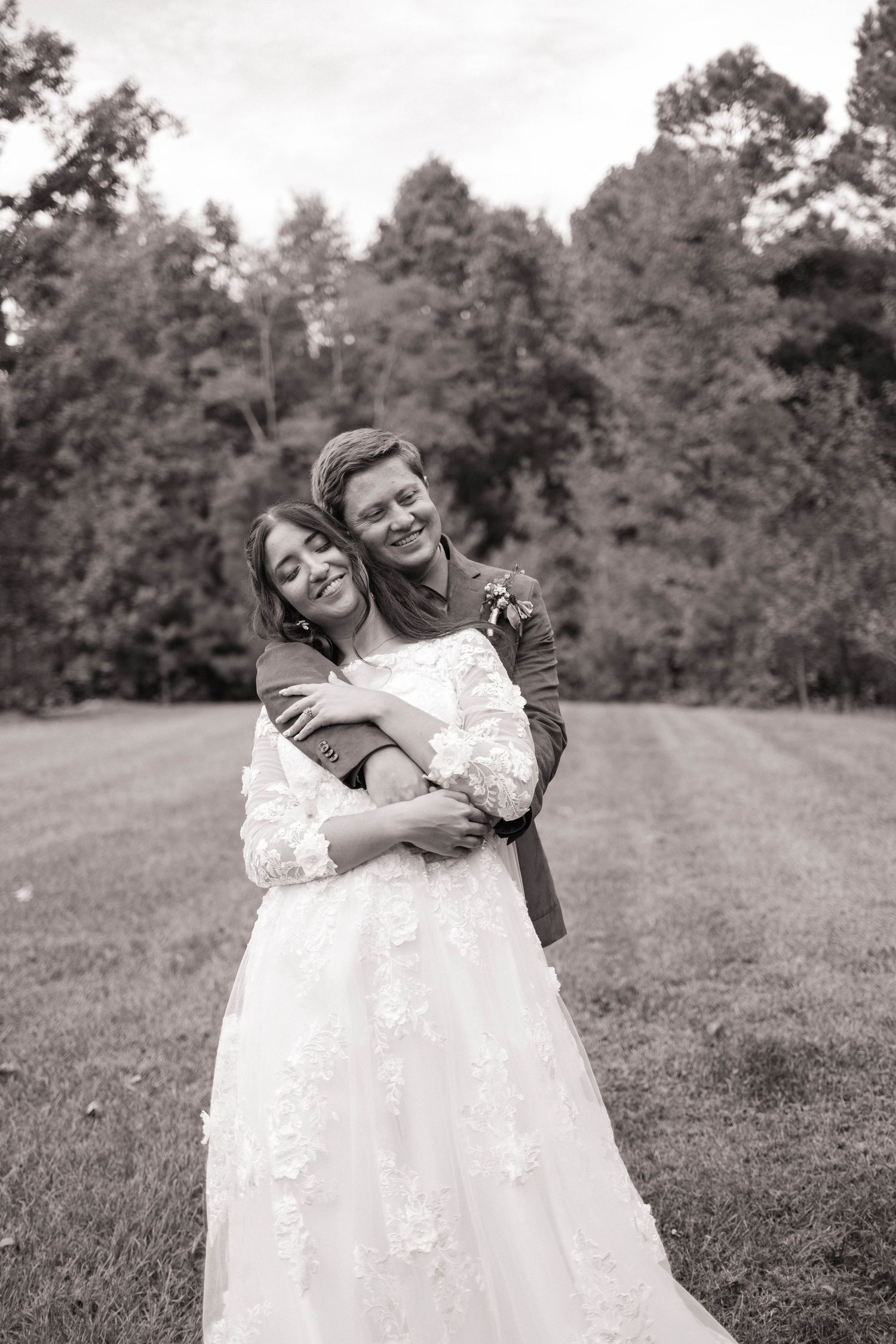 Black and white photo of newlyweds sharing a playful moment on a grassy hill.