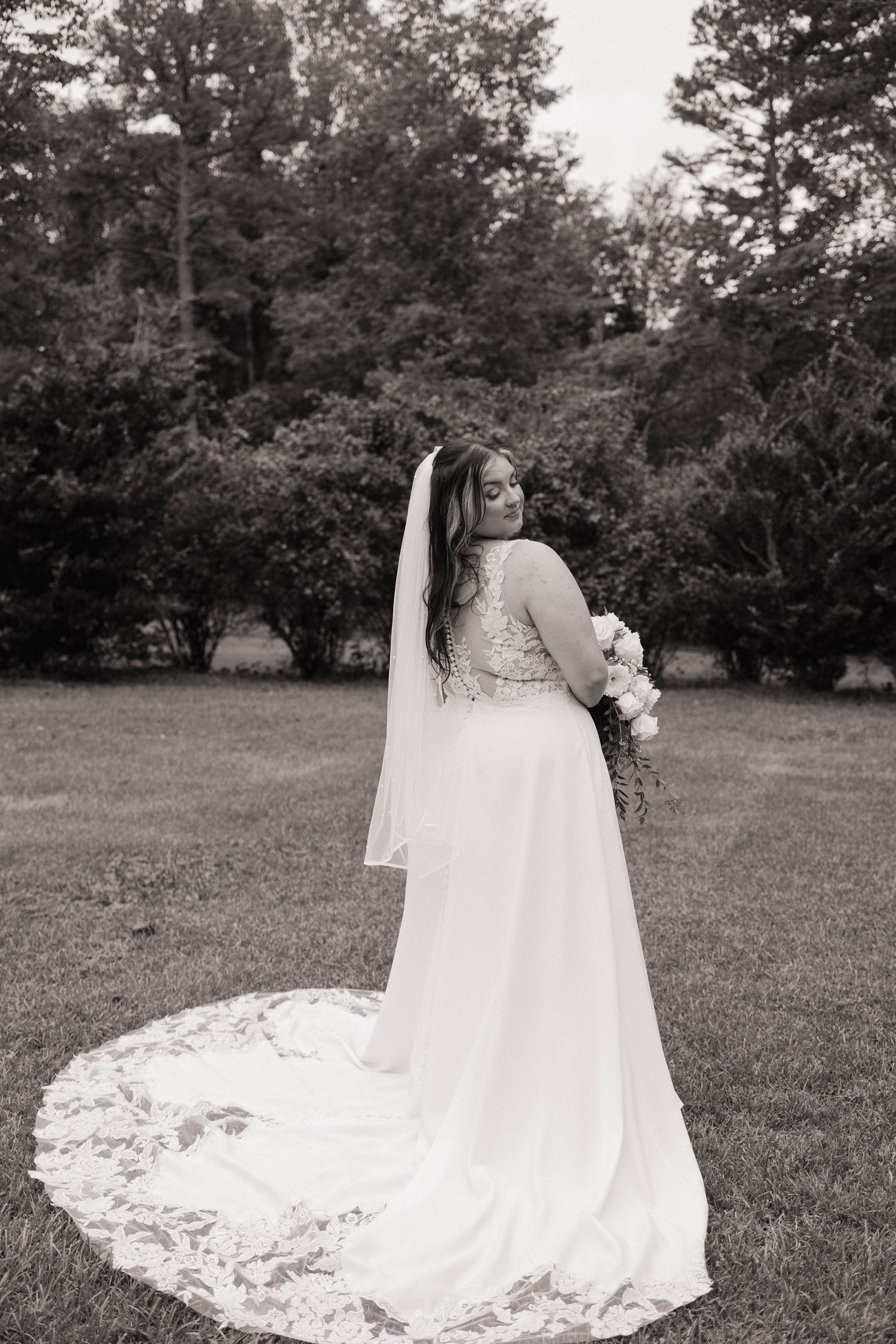 Black and white wedding photo series showing bride's flowing dress train on grassy field.