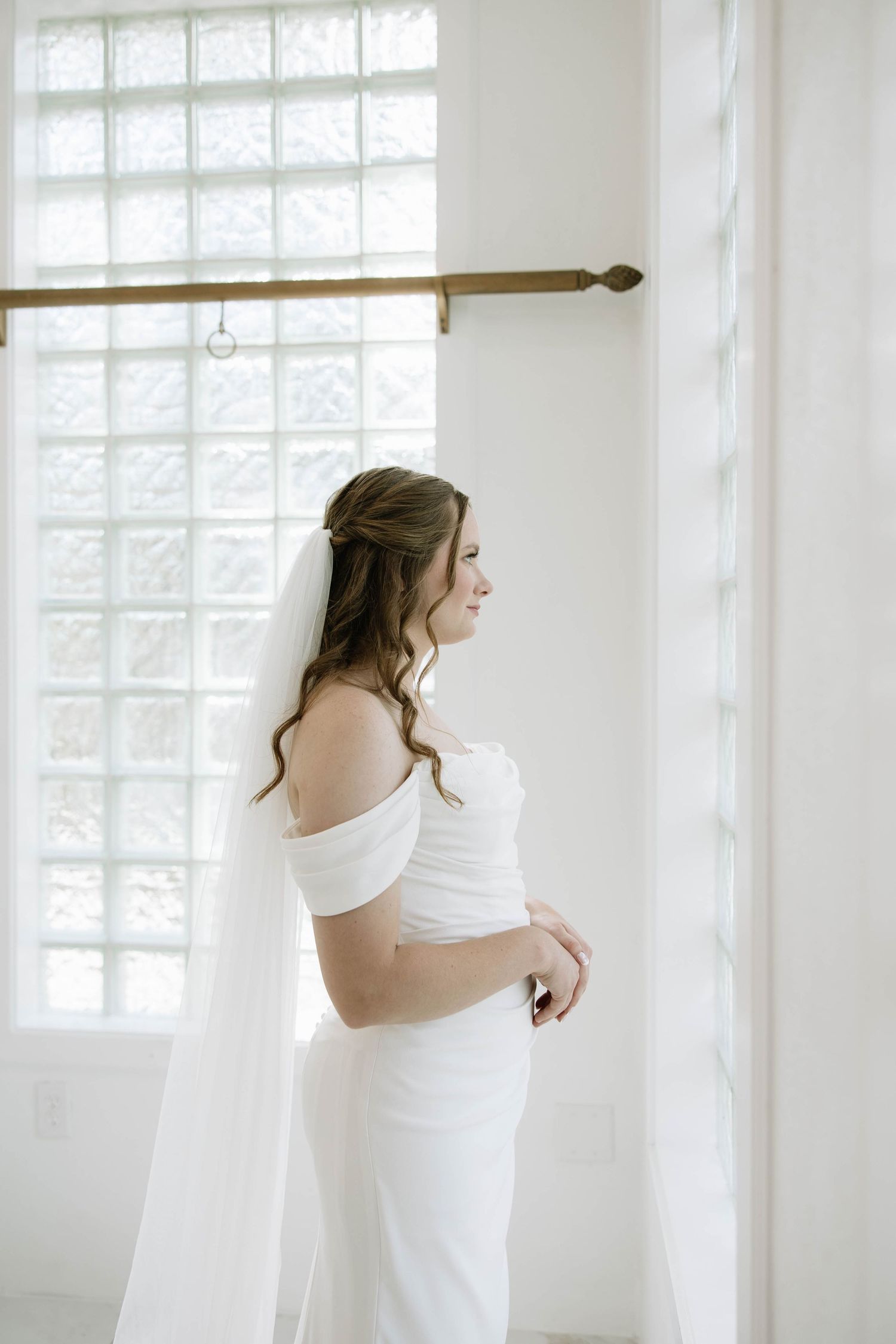 Wedding dress preparation scene in a bright white room with large windows.