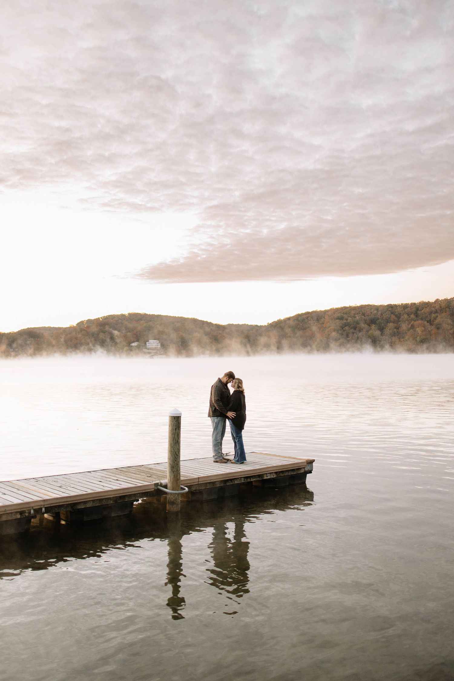 A couple sharing an intimate moment on a misty lake dock at sunrise.