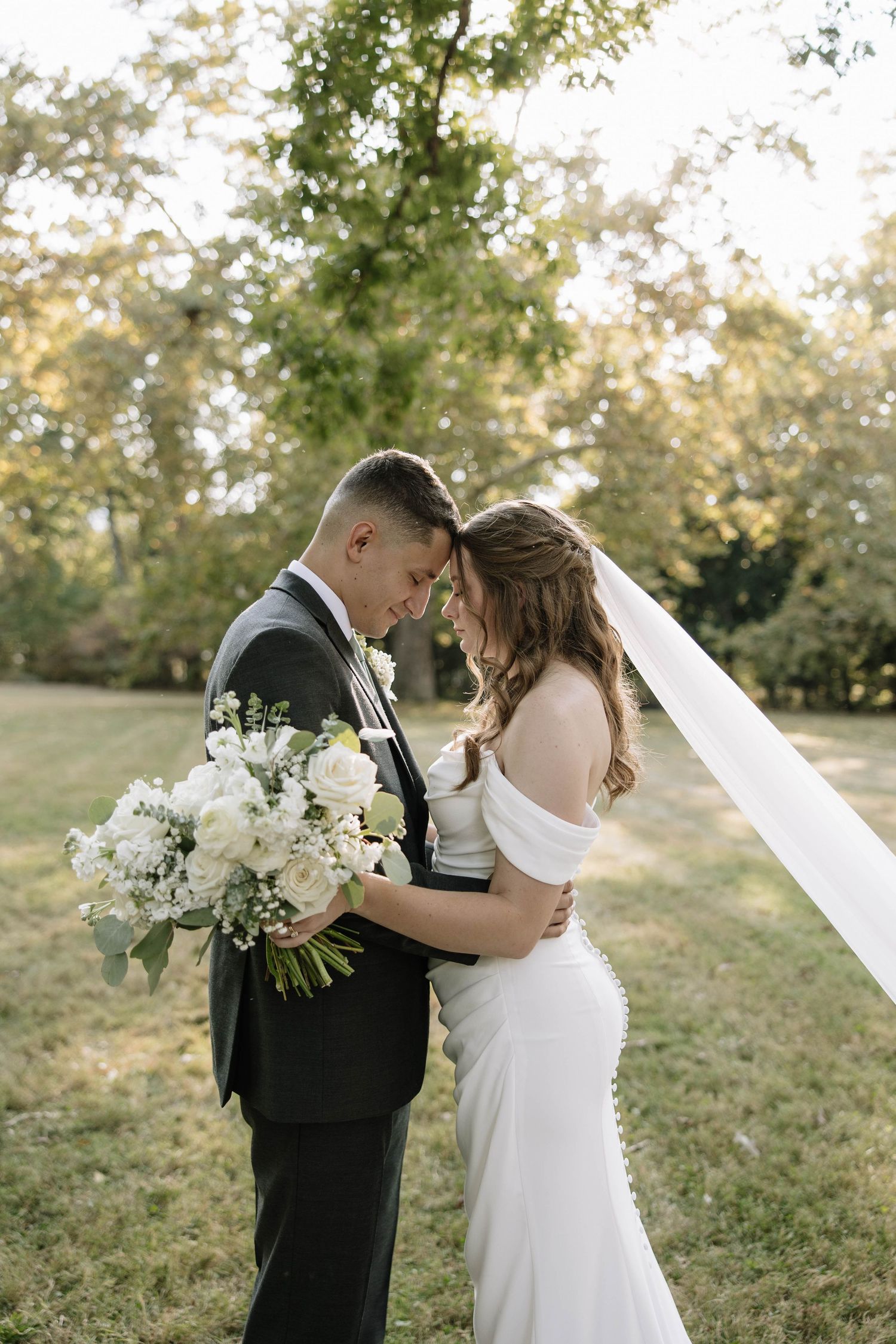 Romantic wedding couple embracing in a garden setting with white floral bouquet.