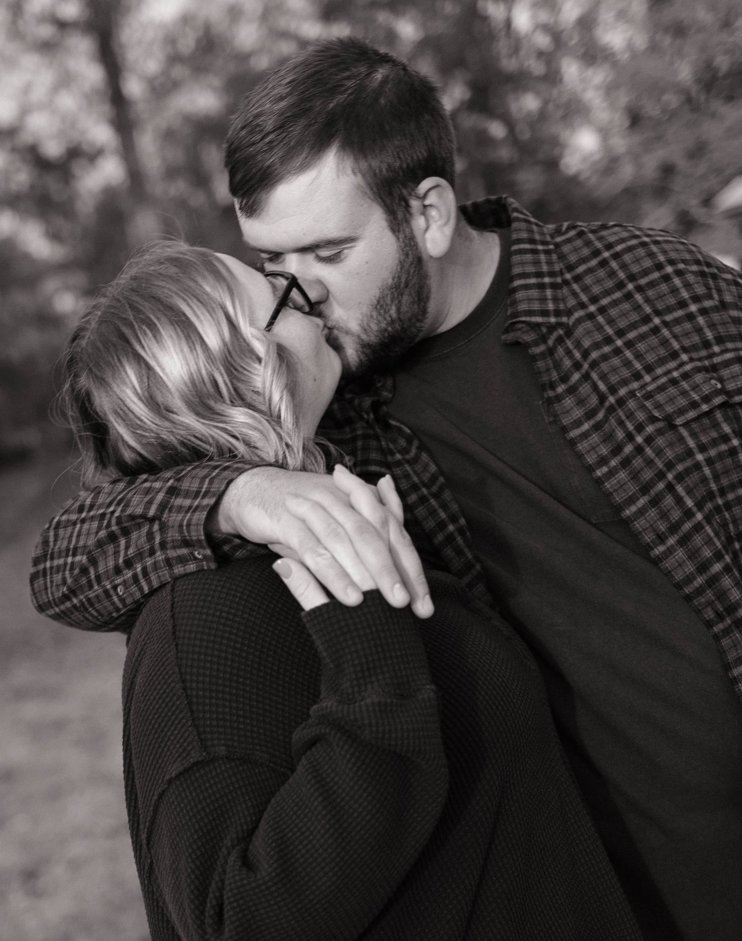 A tender black and white portrait of a couple sharing a kiss outdoors.