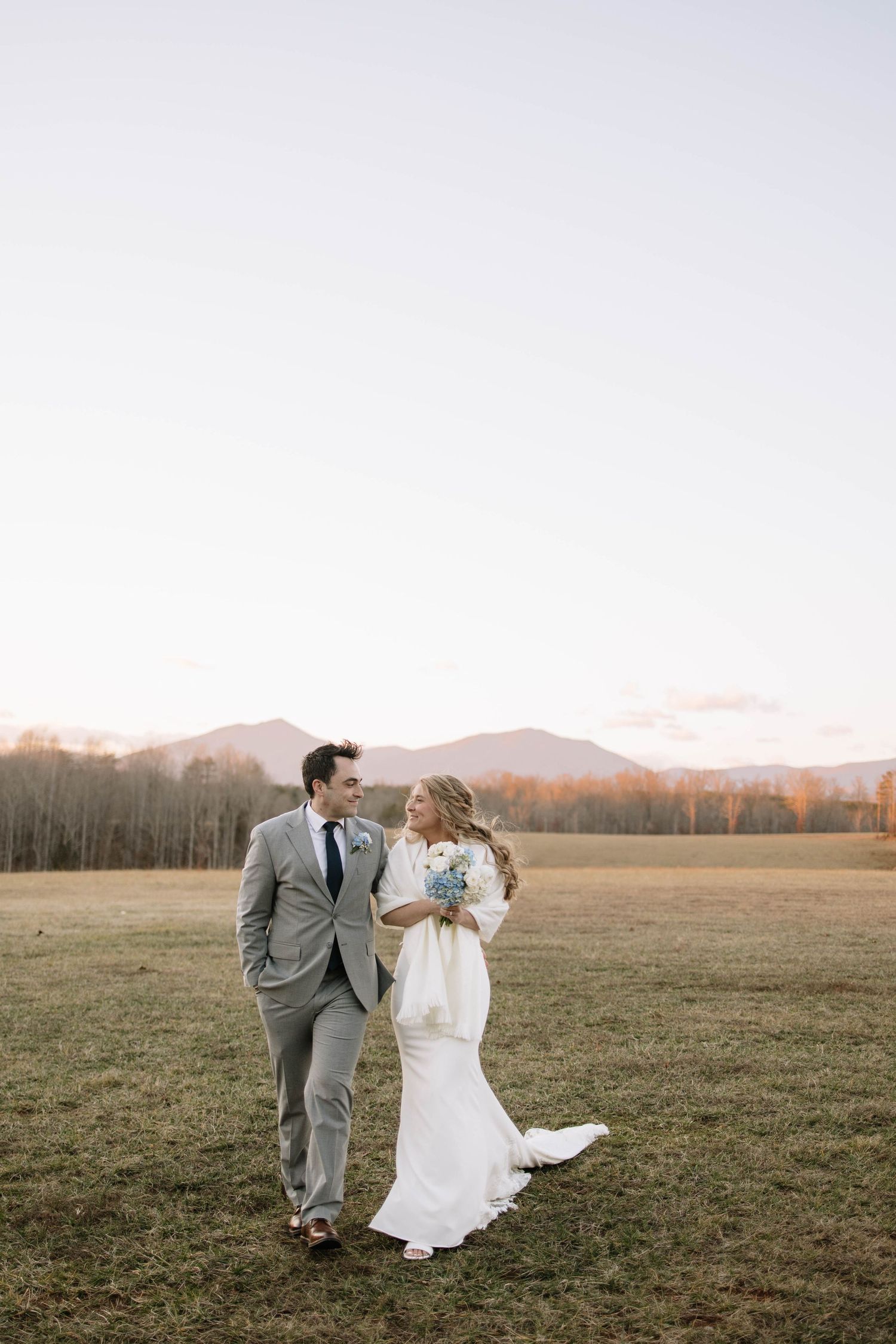 Newlyweds dance and laugh together in open field at golden hour.