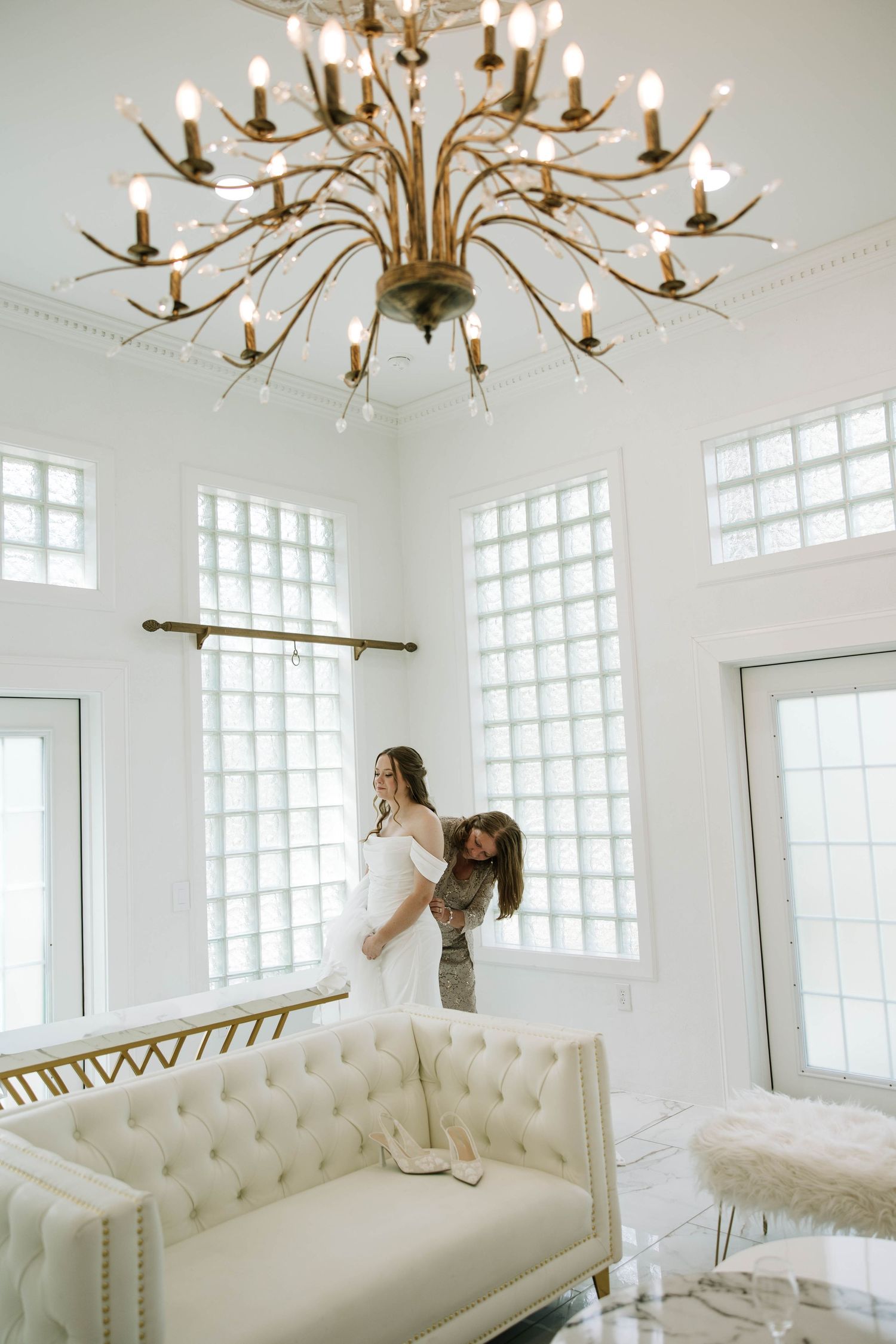 Elegant white studio space with crystal chandelier, tufted white sofa, and glass block windows creating natural light.