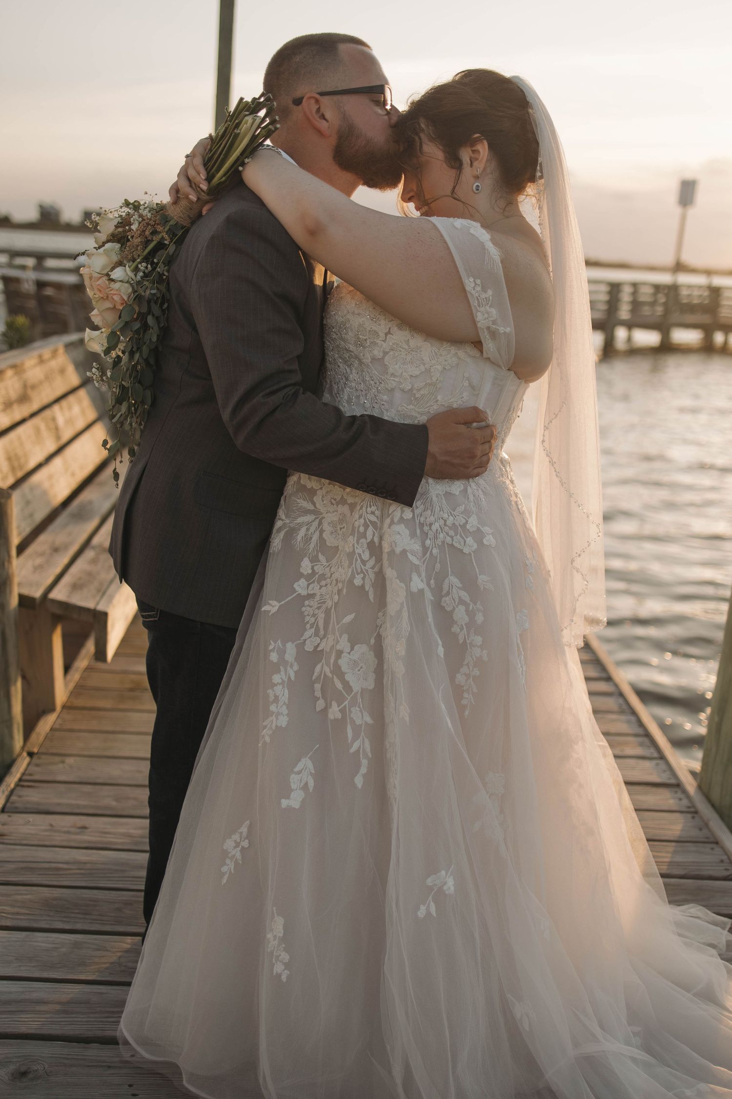 Couple embracing on wooden dock during sunset wedding photoshoot.