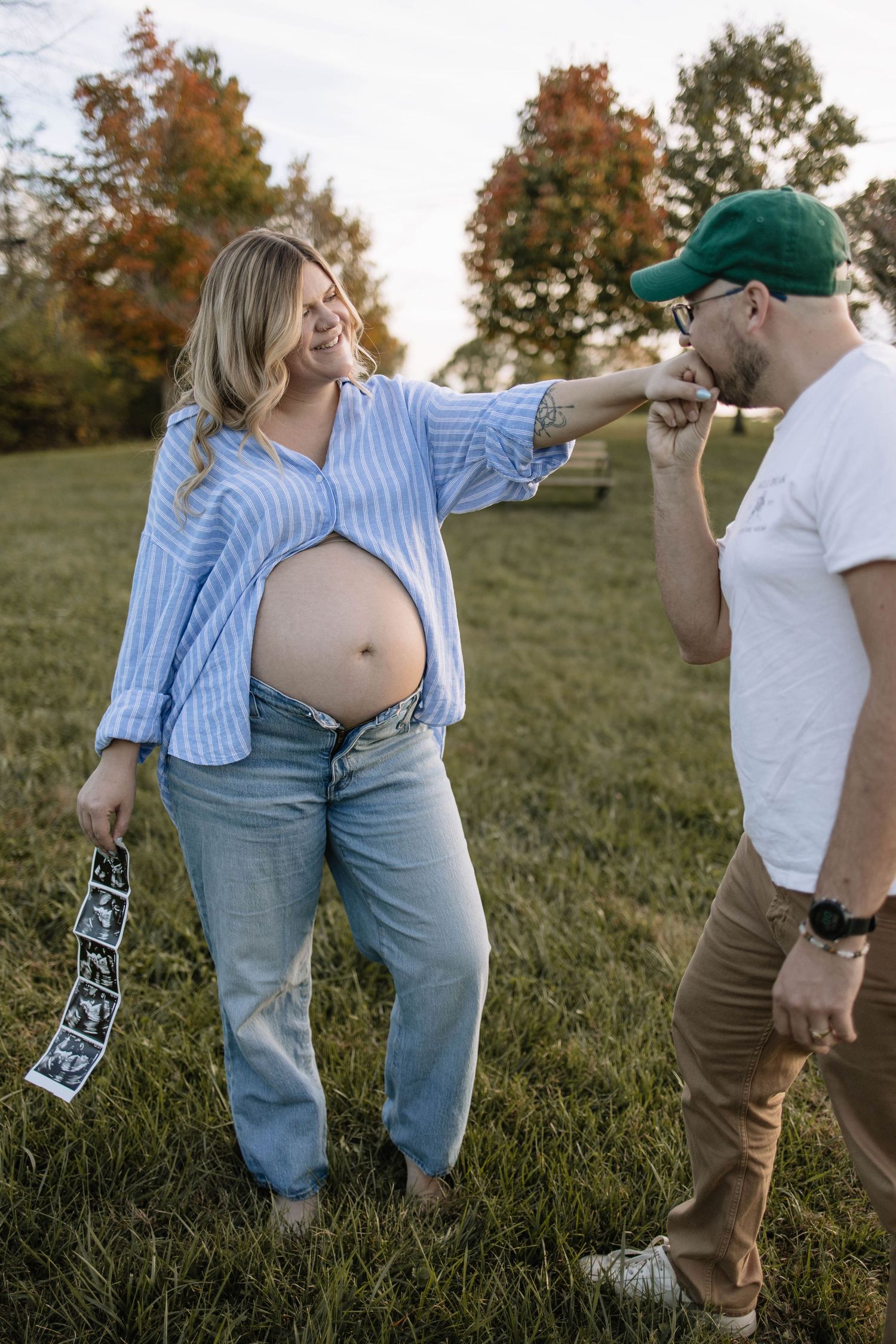 Playful maternity photo session in a grassy field during golden hour.