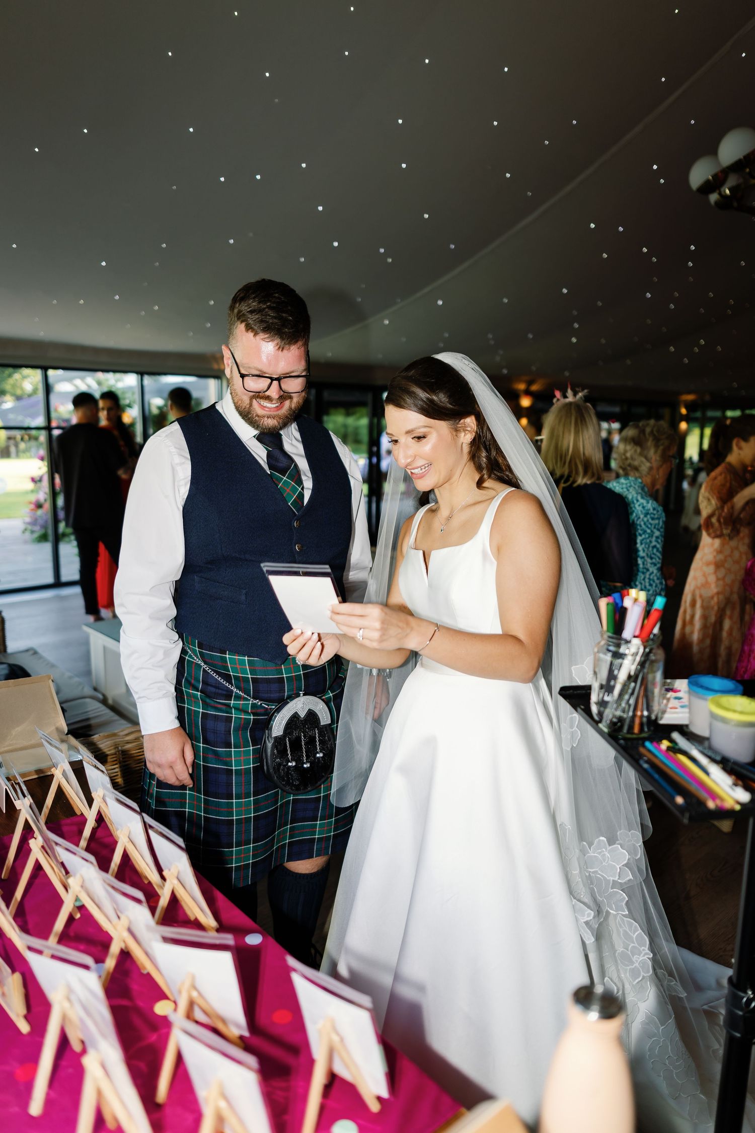 A couple dances together during a wedding reception while guests sit at tables with pink chairs in the background.