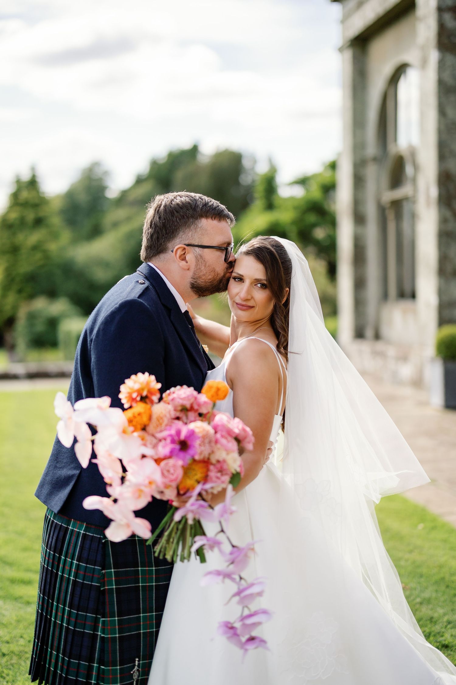 “Newlyweds walking through the gardens of Kinmount House in Scotland, surrounded by natural greenery and timeless architecture.”