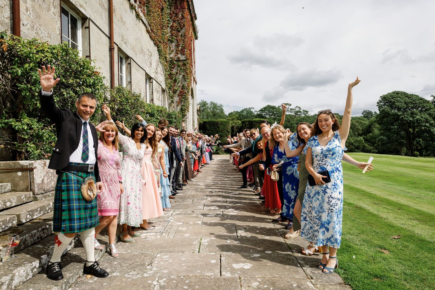 Wedding guests lined up outside a historic stone building create a celebratory walkway for the newlyweds.