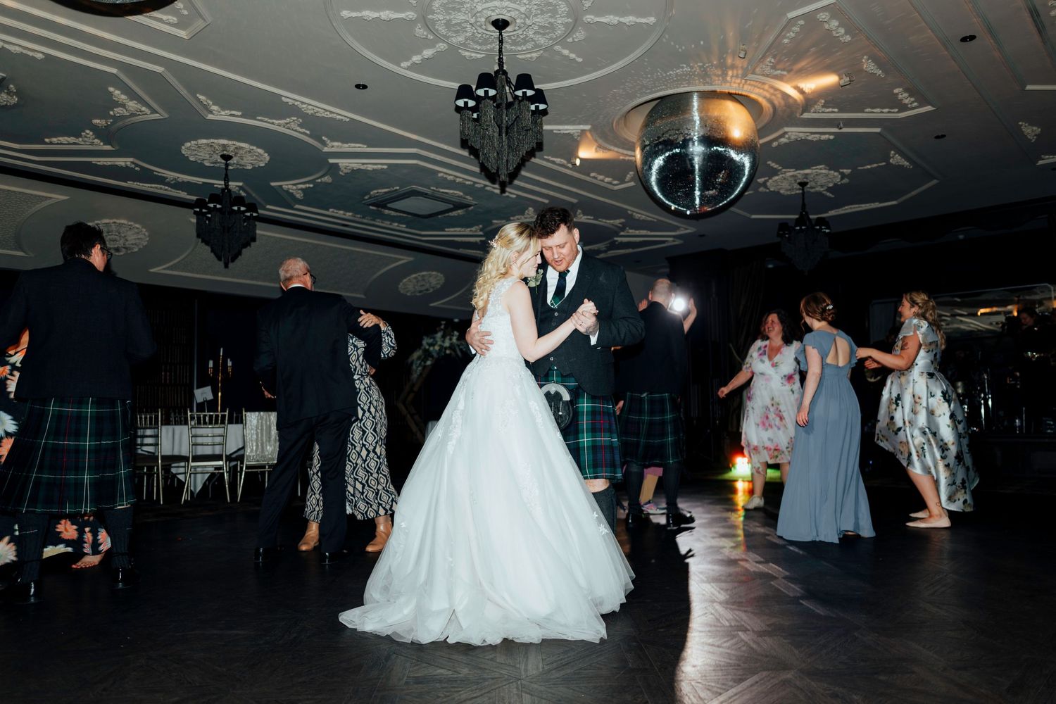Wedding guests dancing on the dance floor under elegant chandeliers at an evening reception celebration.