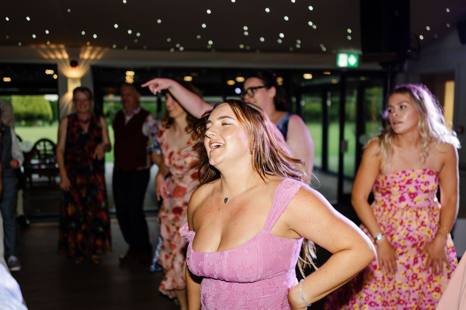 A group of people dancing together at a party wearing pink and floral dresses.