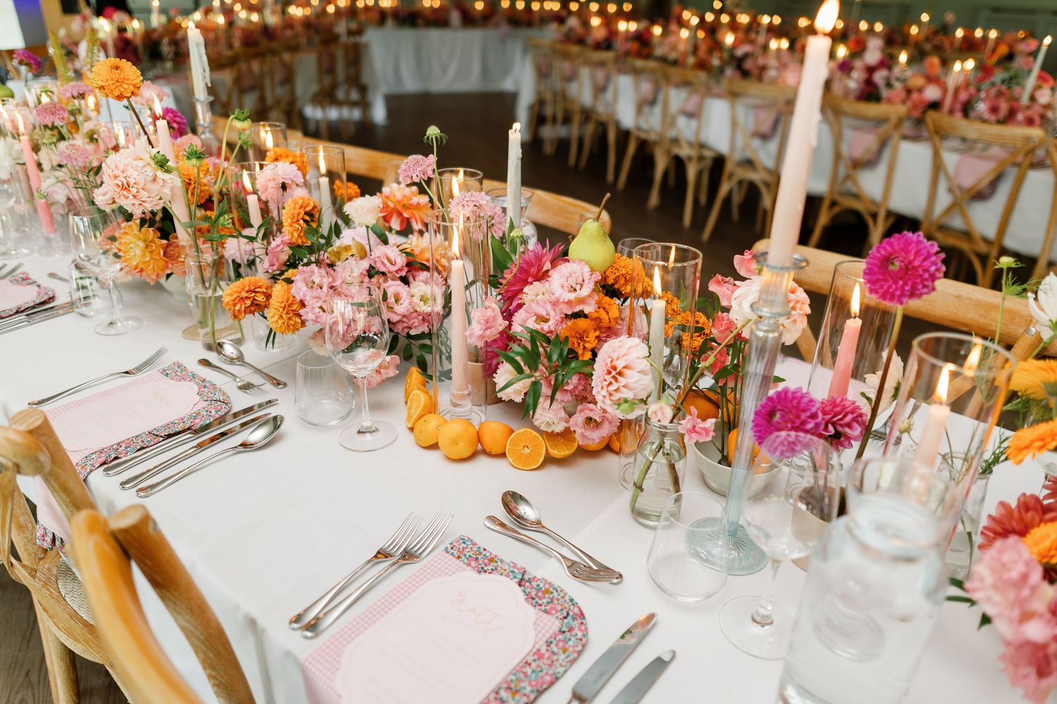 Elegant wedding reception tables decorated with vibrant floral centerpieces, candles and place settings under string lights.