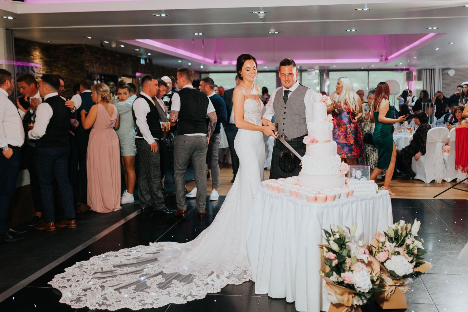 Couple shares their first dance at wedding reception with stunning white dress train and purple uplighting.