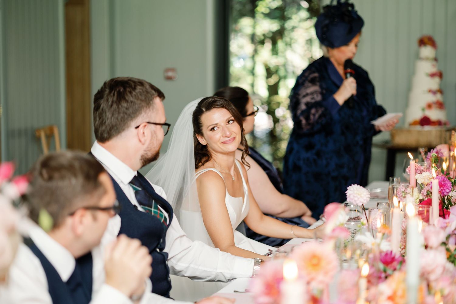 Wedding guests seated at an elegant reception table with pink floral centerpieces and candlelight.