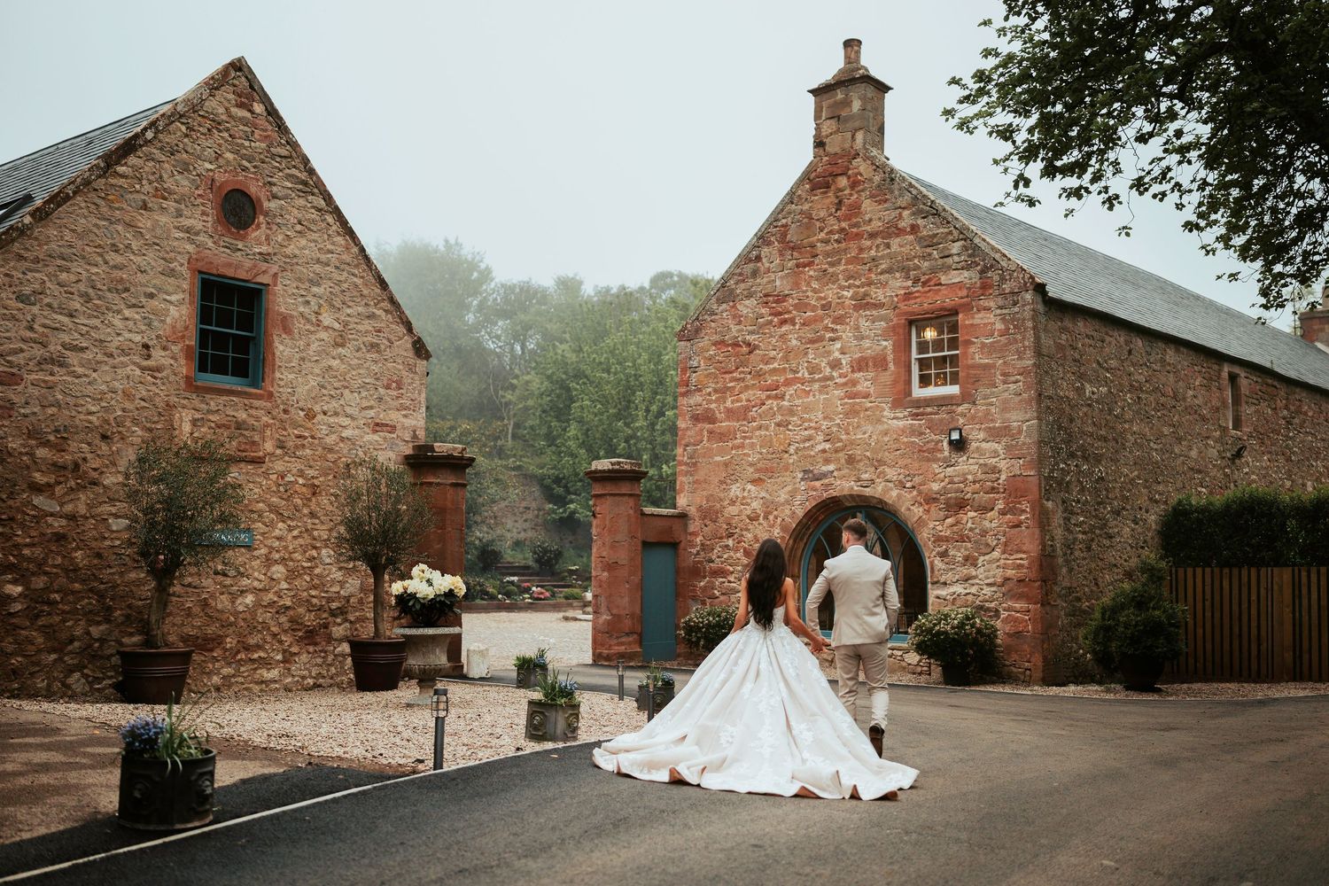 A series of rustic brick buildings and barns arranged in a panoramic sequence showing a wedding venue setting.