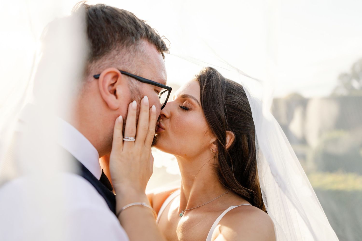 A romantic couple shares tender kisses in an outdoor setting with soft natural lighting.