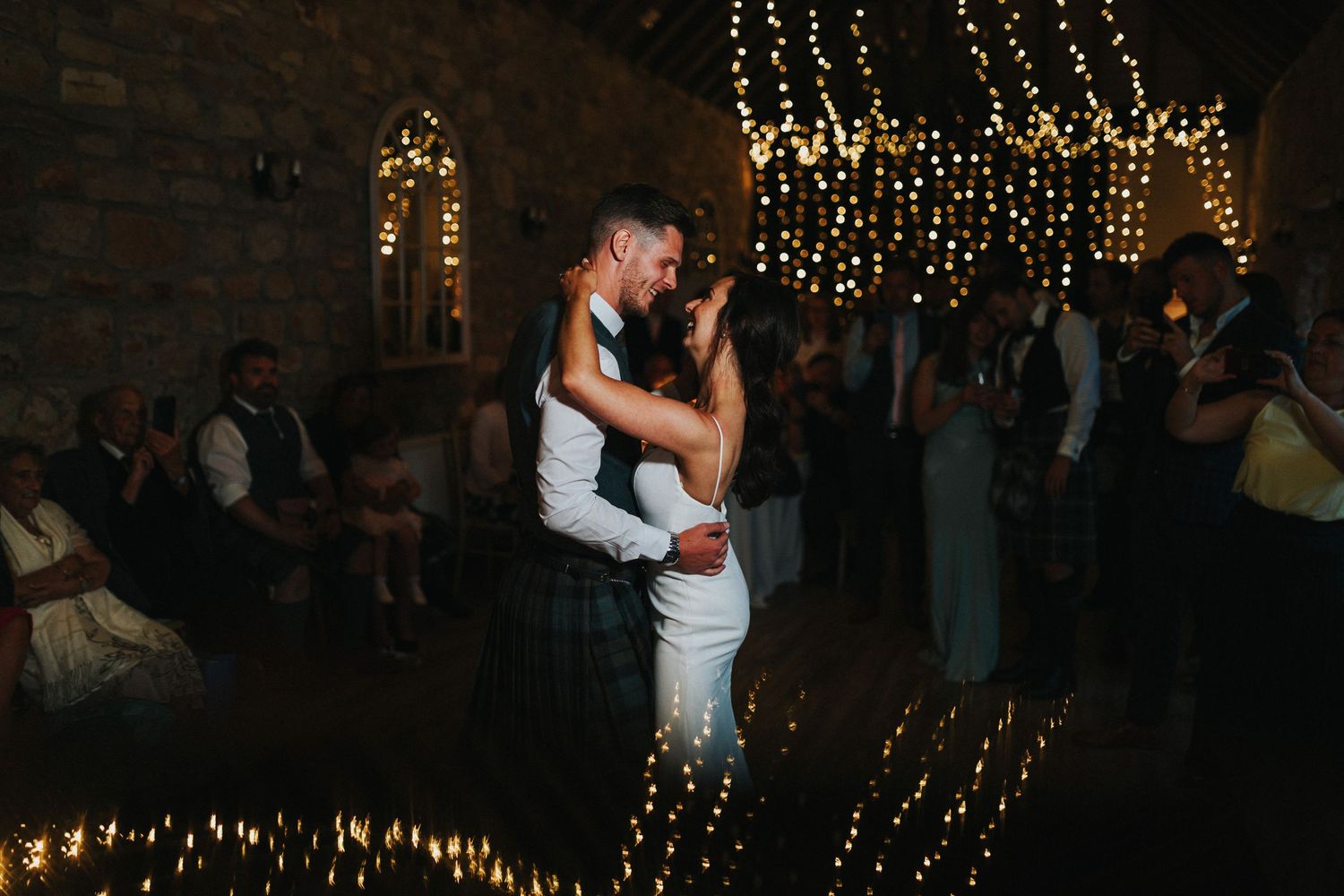 A couple shares their first dance under twinkling string lights at an intimate indoor wedding reception.