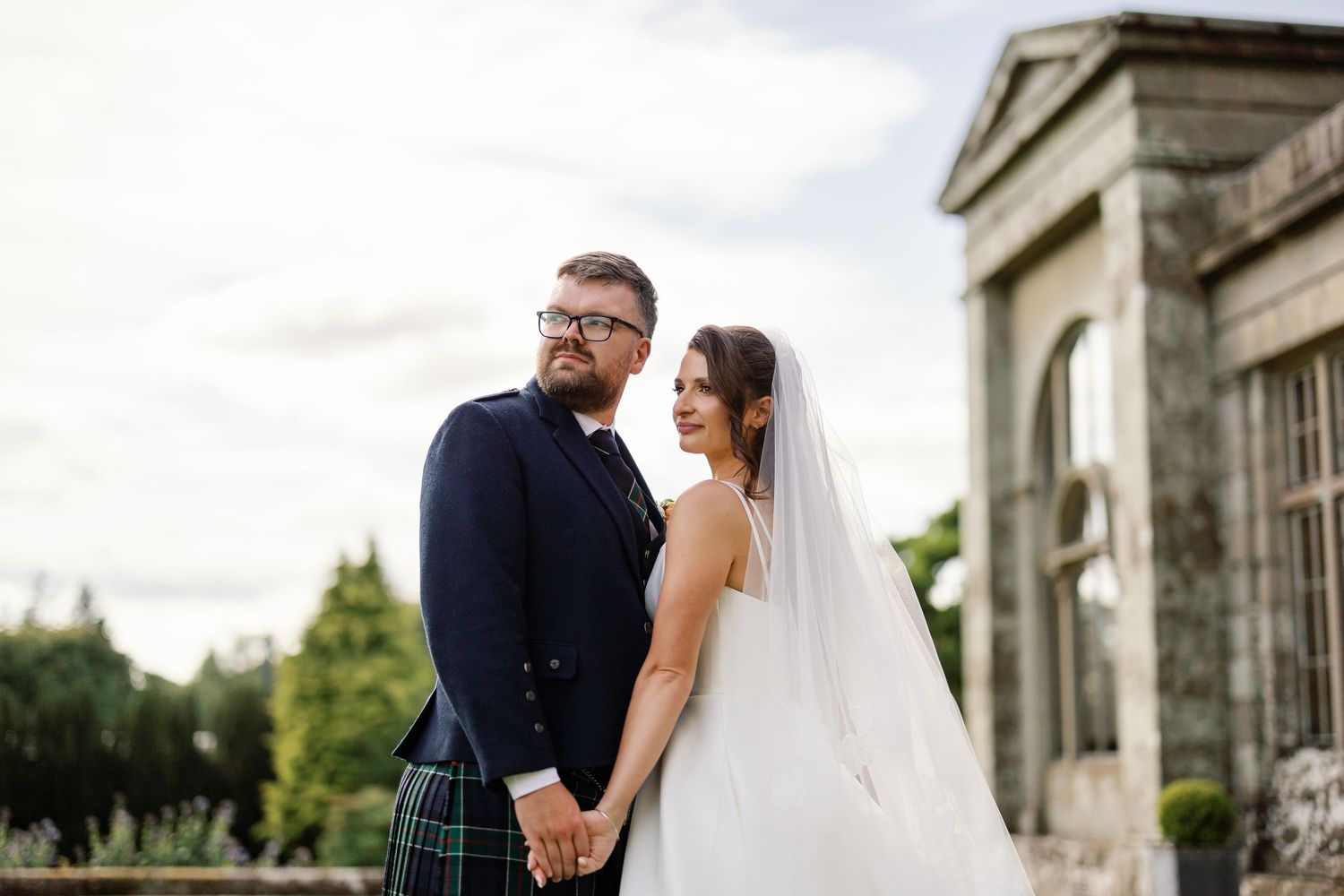 “Bride and groom standing in front of Kinmount House, a stately Scottish mansion with sweeping lawns and classic architecture.