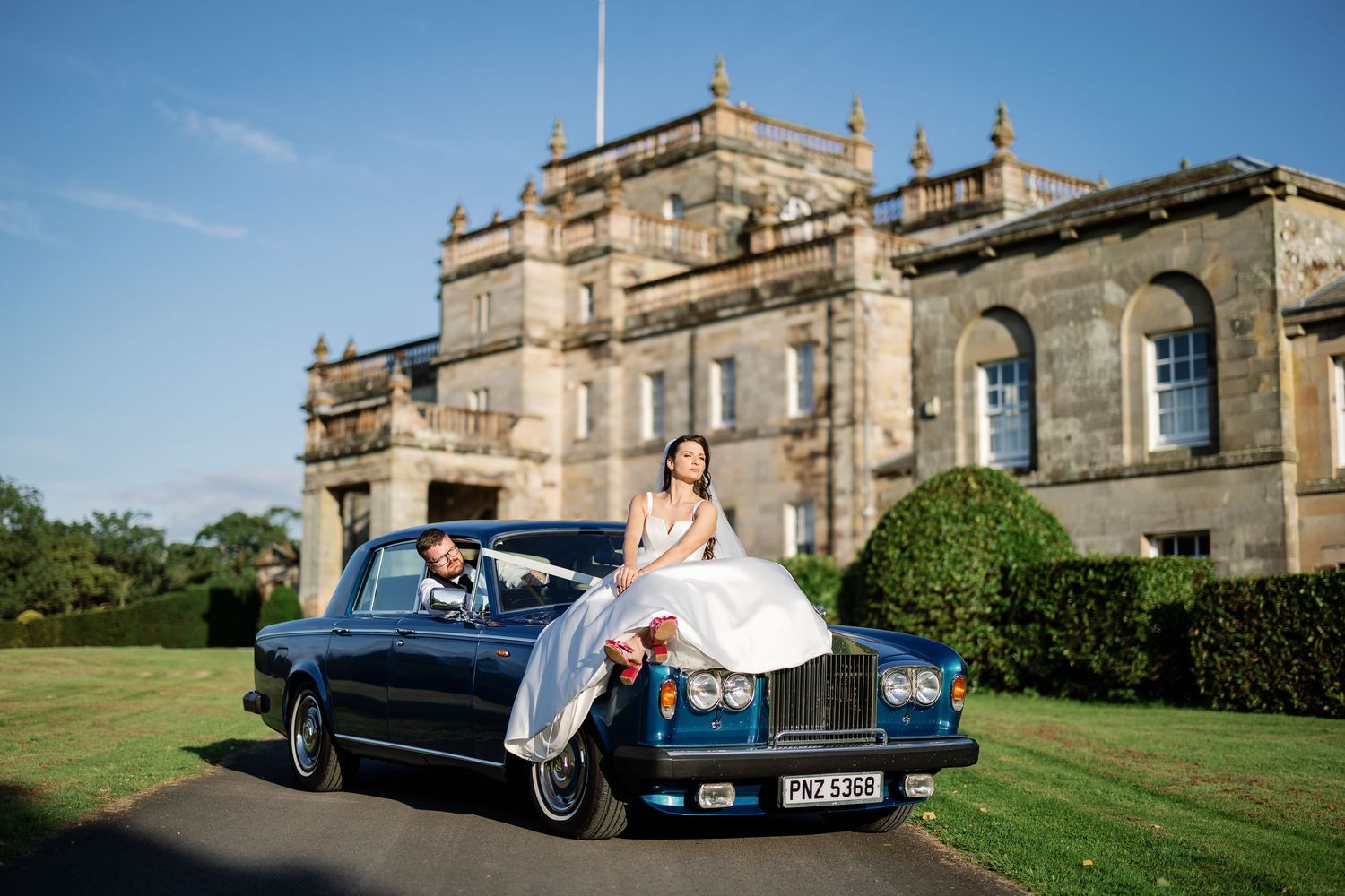 “Bride and groom standing in front of Kinmount House, a stately Scottish mansion with sweeping lawns and classic architecture.”