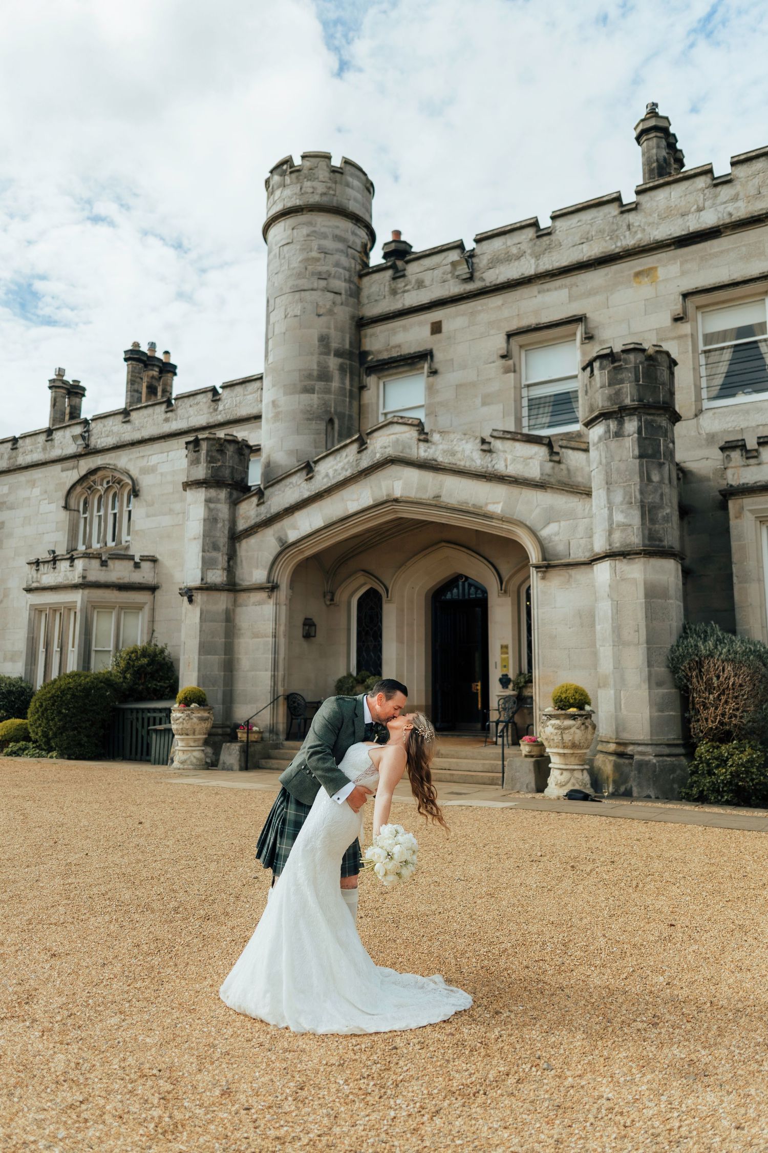 Newlyweds share romantic dip kiss outside grand castle wedding venue with stone architecture. Dundas Castle Wedding