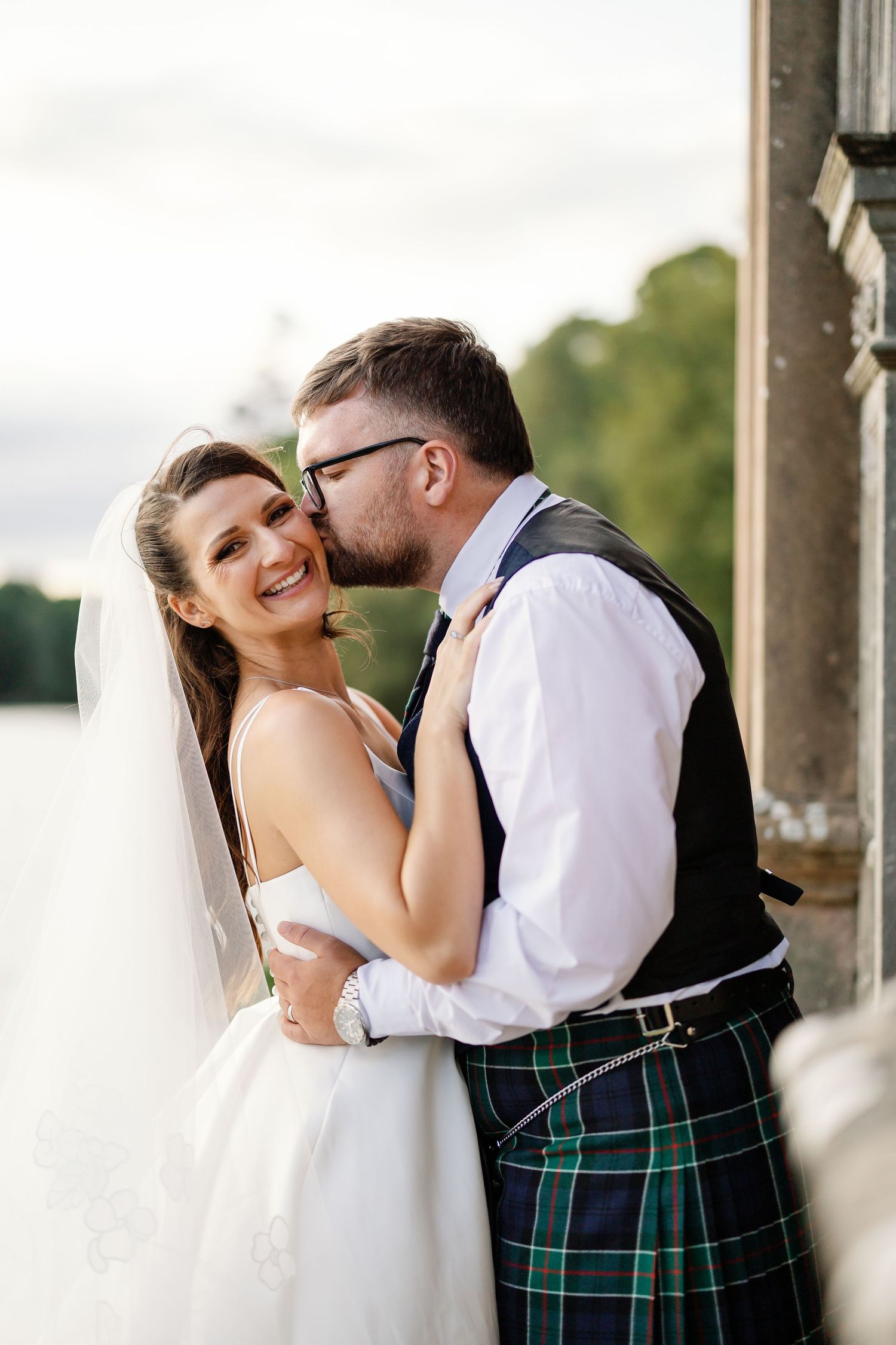 “Bride and groom standing in front of Kinmount House, a stately Scottish mansion with sweeping lawns and classic architecture.”