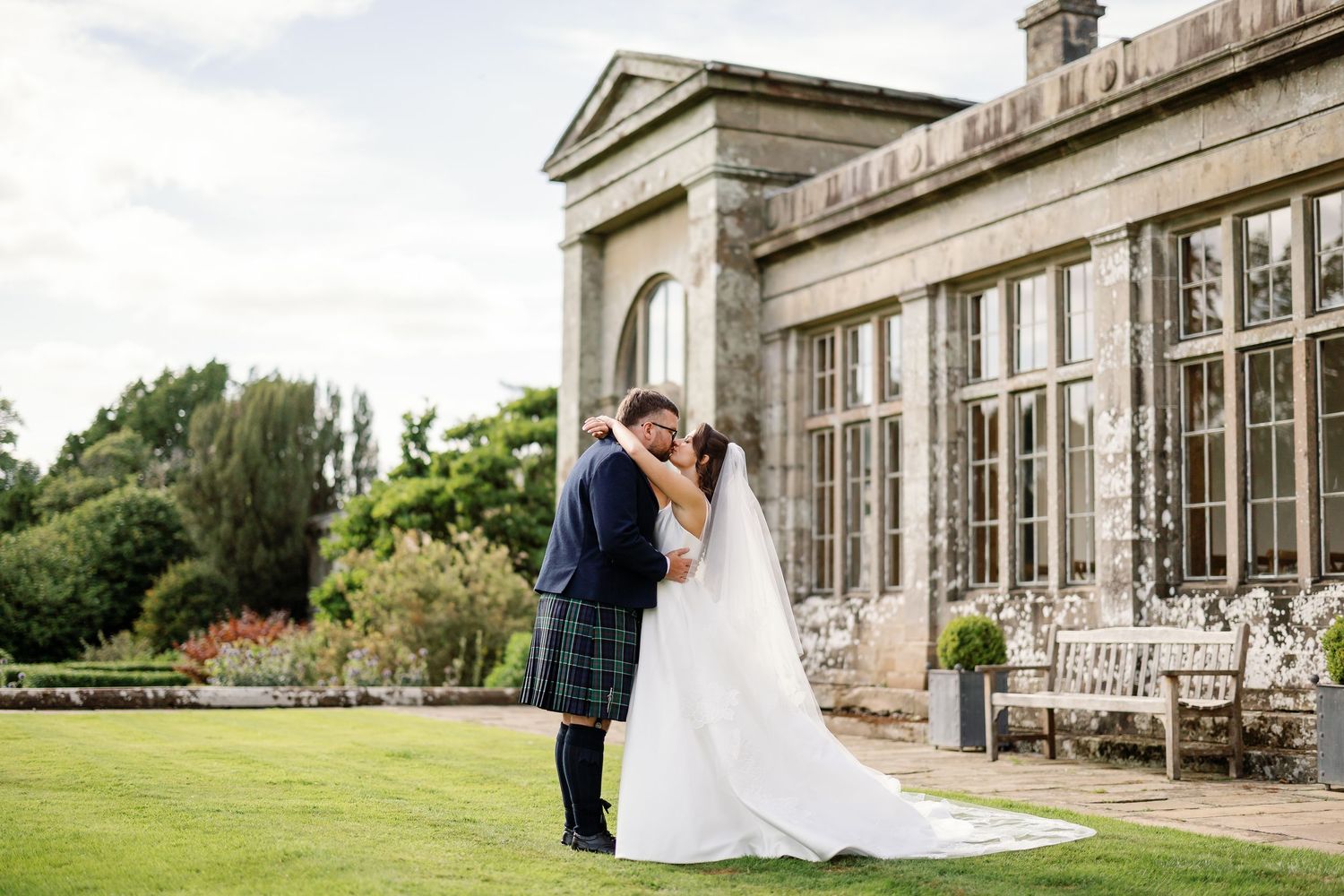 “Bride and groom standing in front of Kinmount House, a stately Scottish mansion with sweeping lawns and classic architecture.”