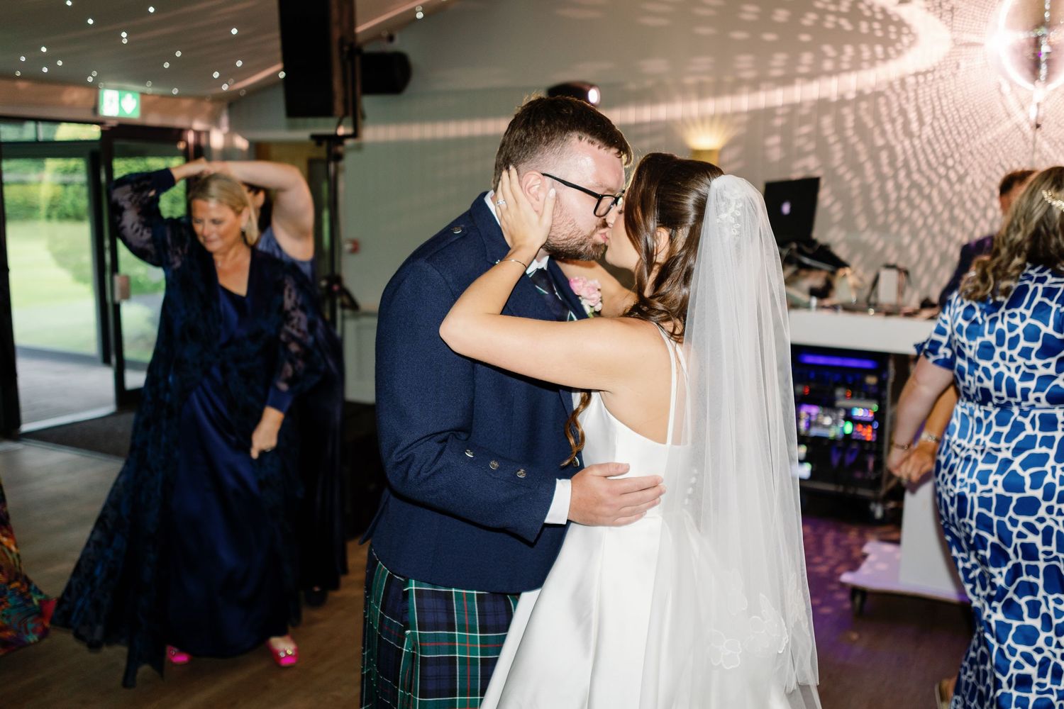 A couple shares their first dance at a wedding reception while guests look on in the background.