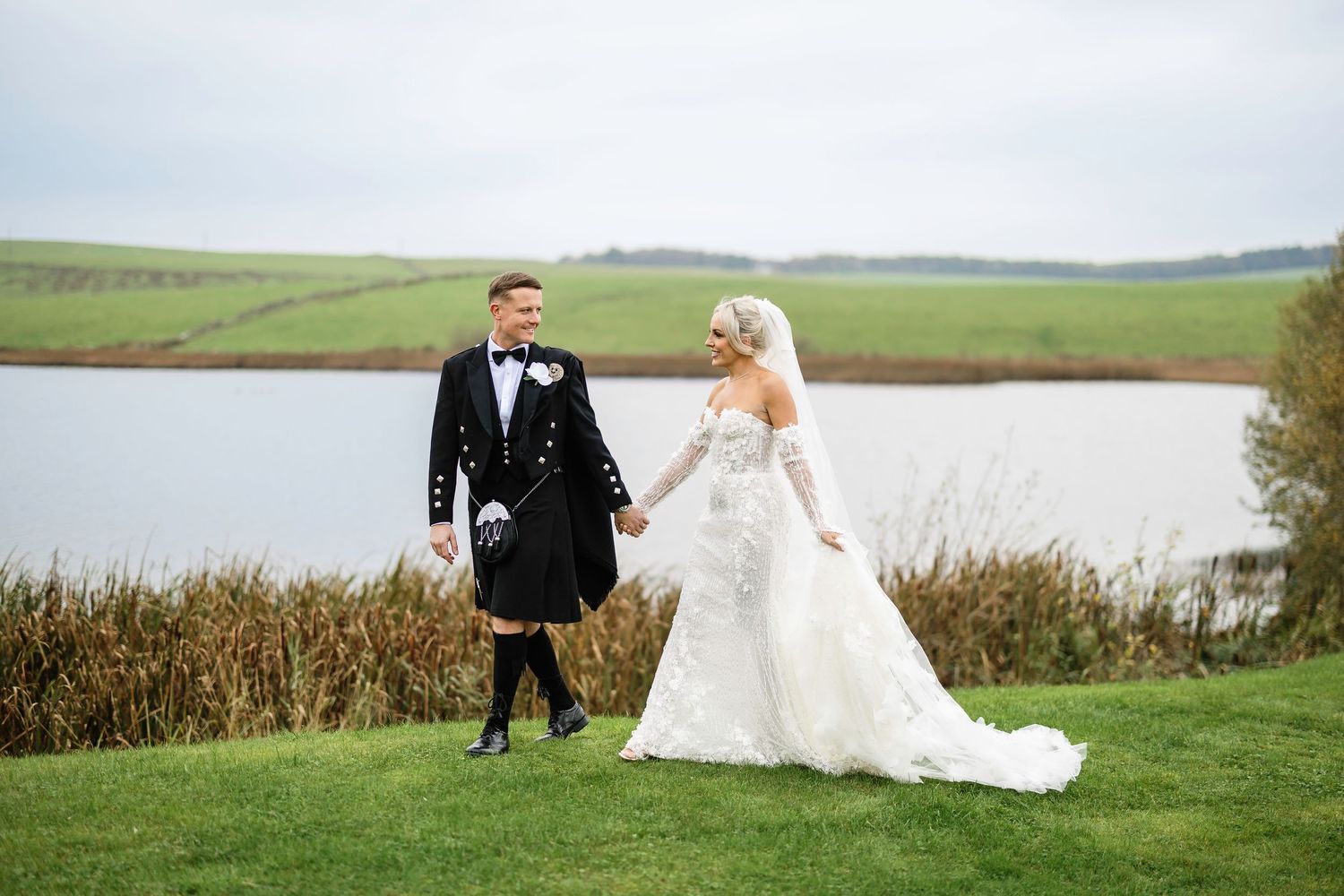 Newlywed couple walks together through scenic rural fields on their wedding day.