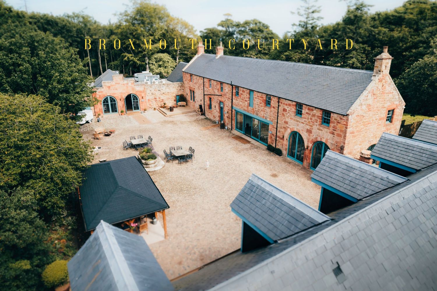 Aerial view of a renovated brick courtyard with outdoor seating and slate roofs at a luxury hospitality venue.