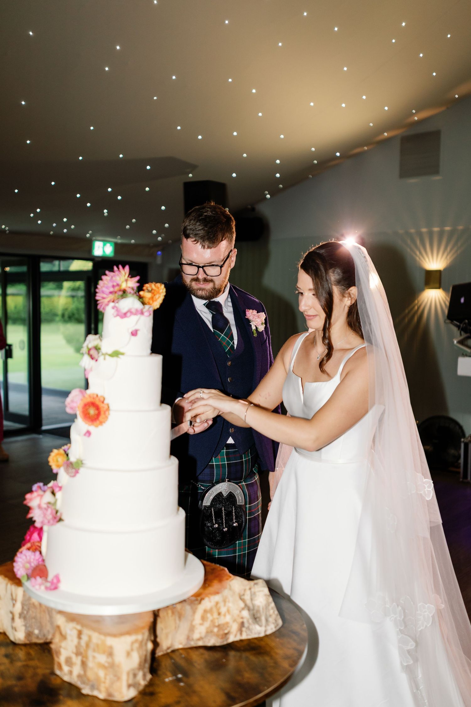 A series of five wedding photos showing a couple cutting and feeding each other bites of their elegant floral-decorated white cake.