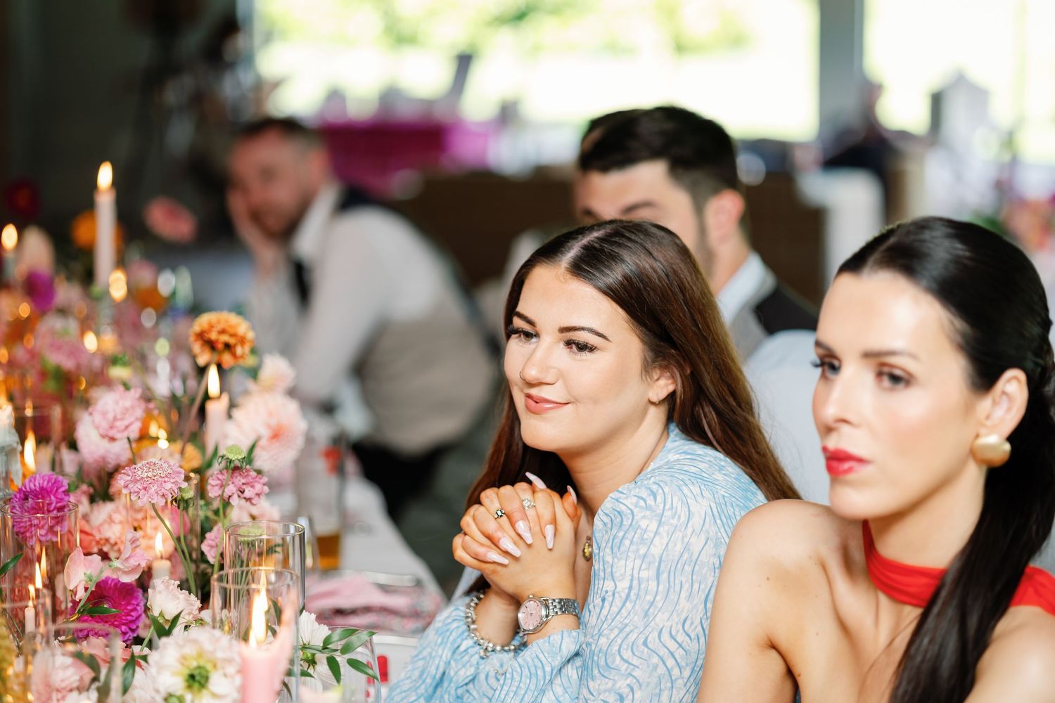 Wedding reception guests seated at elegant tables with pink floral centerpieces enjoying a formal celebration.