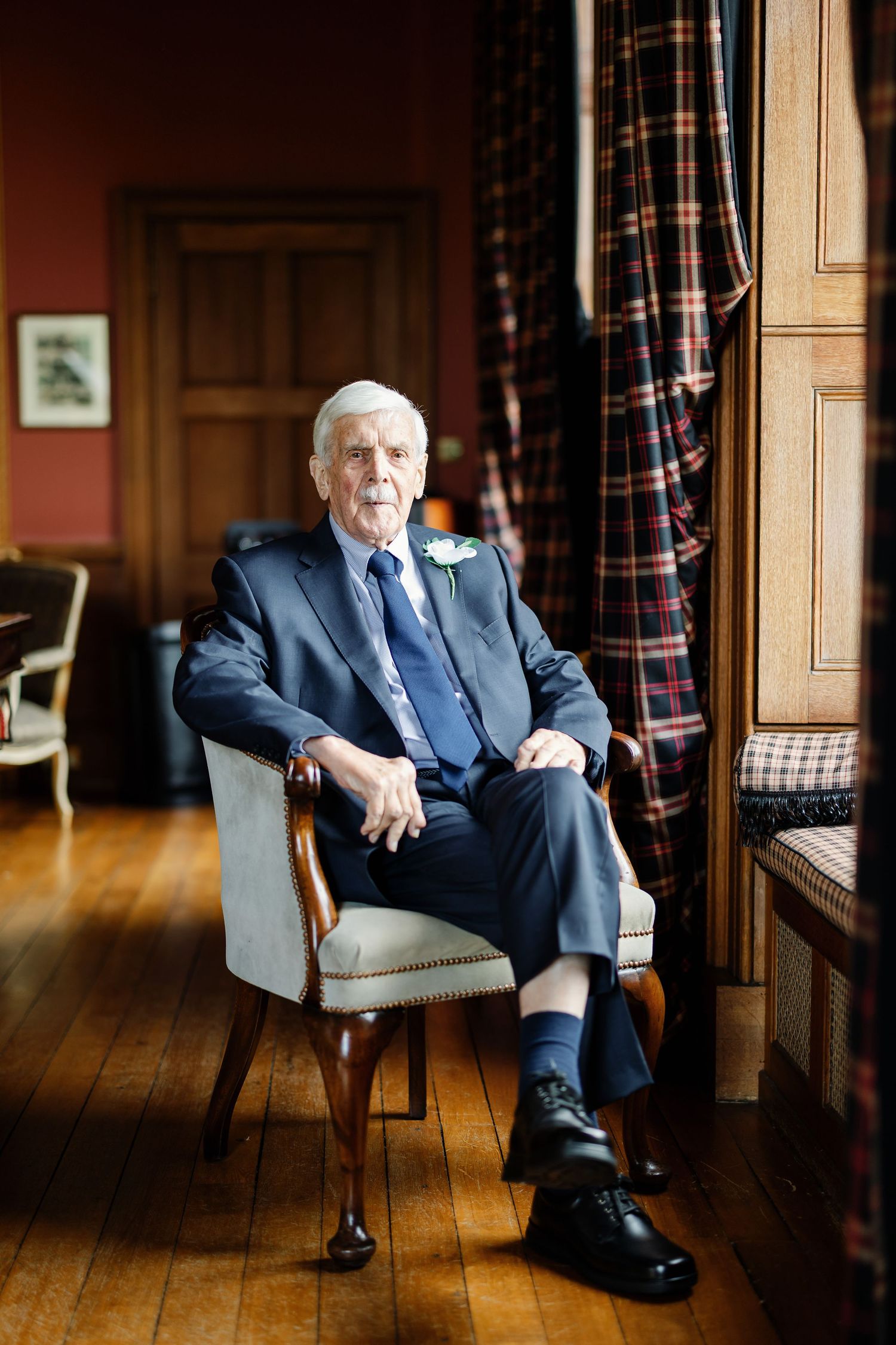A sequence of four photos showing someone seated in a formal navy suit on a leather chair against wood paneled walls.
