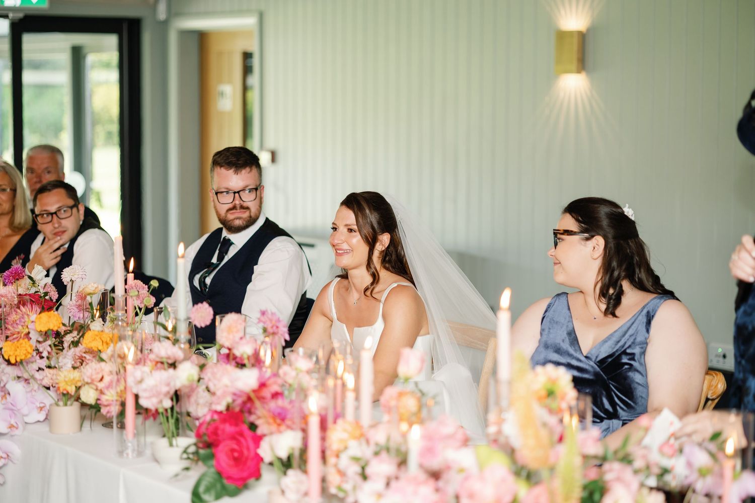Wedding guests enjoy a festive reception dinner at decorated tables with pink floral centerpieces and glowing candlelight.