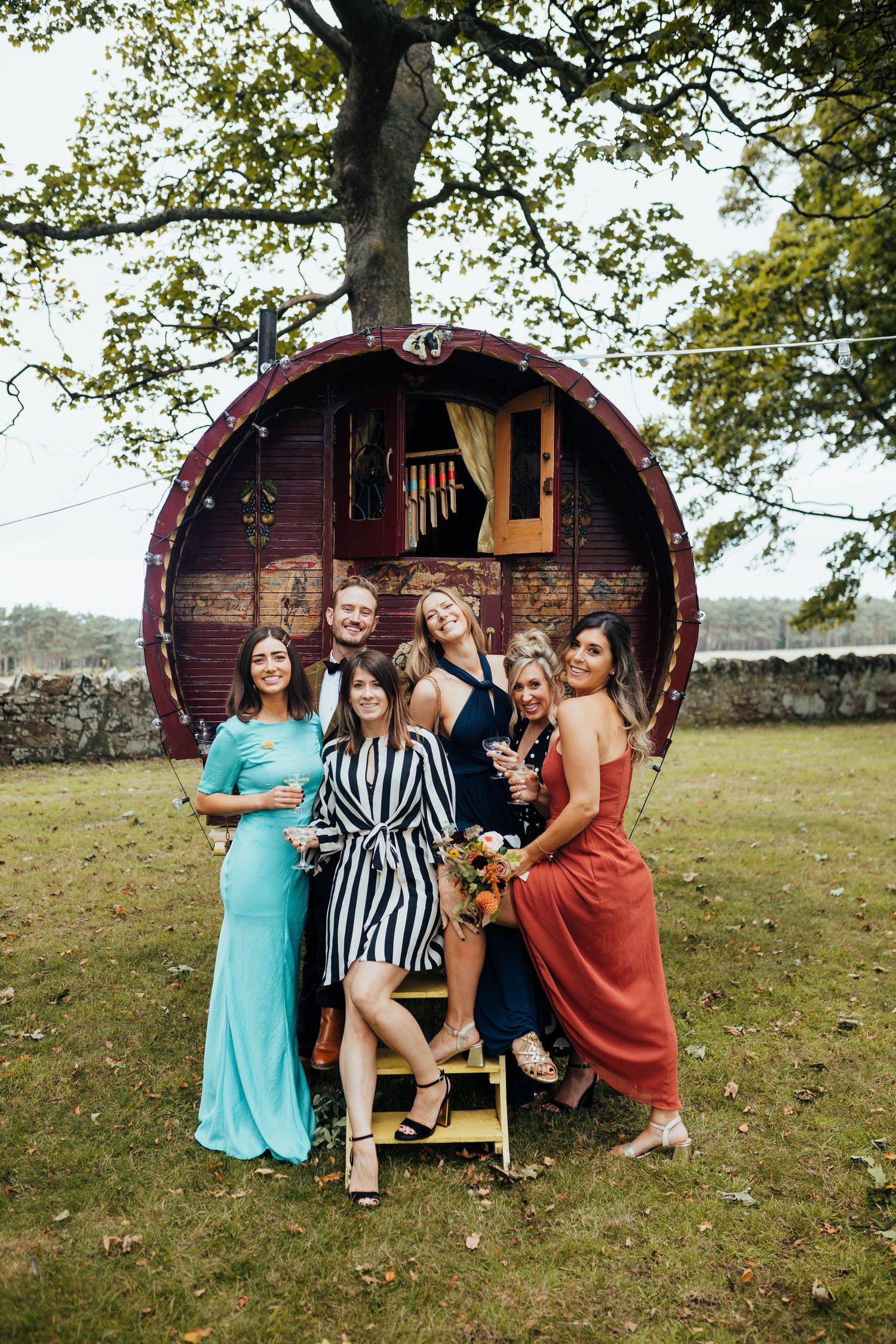 A group stands together in front of a large circular wooden structure decorated with an American flag in a grassy field.