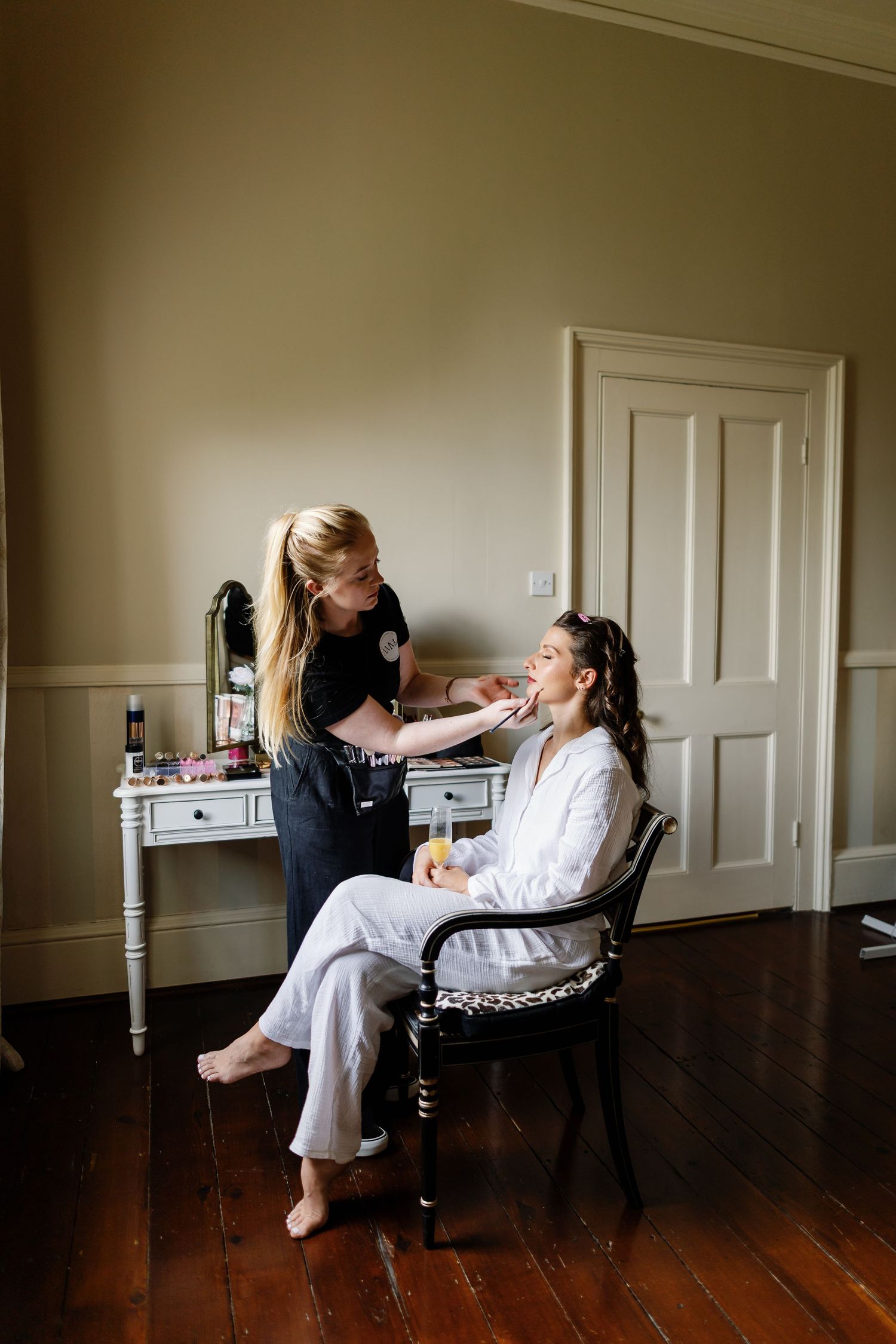 A series of photos showing a makeup artist applying cosmetics to a client in a bright room with hardwood floors.